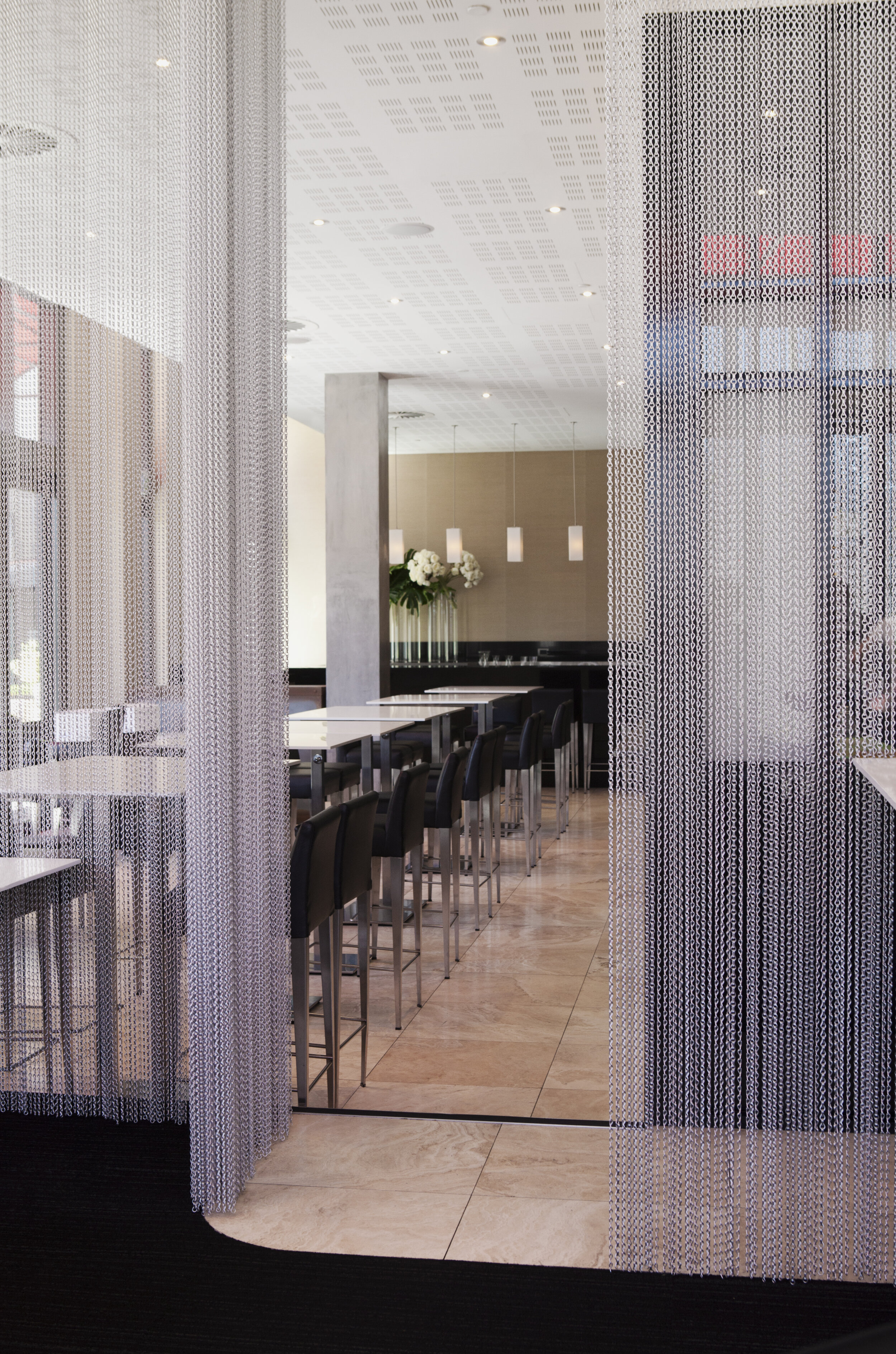 Contemporary hospitality interior featuring decorative chain curtains, custom dining seating and architectural detailing by Luis La Pegna Designs