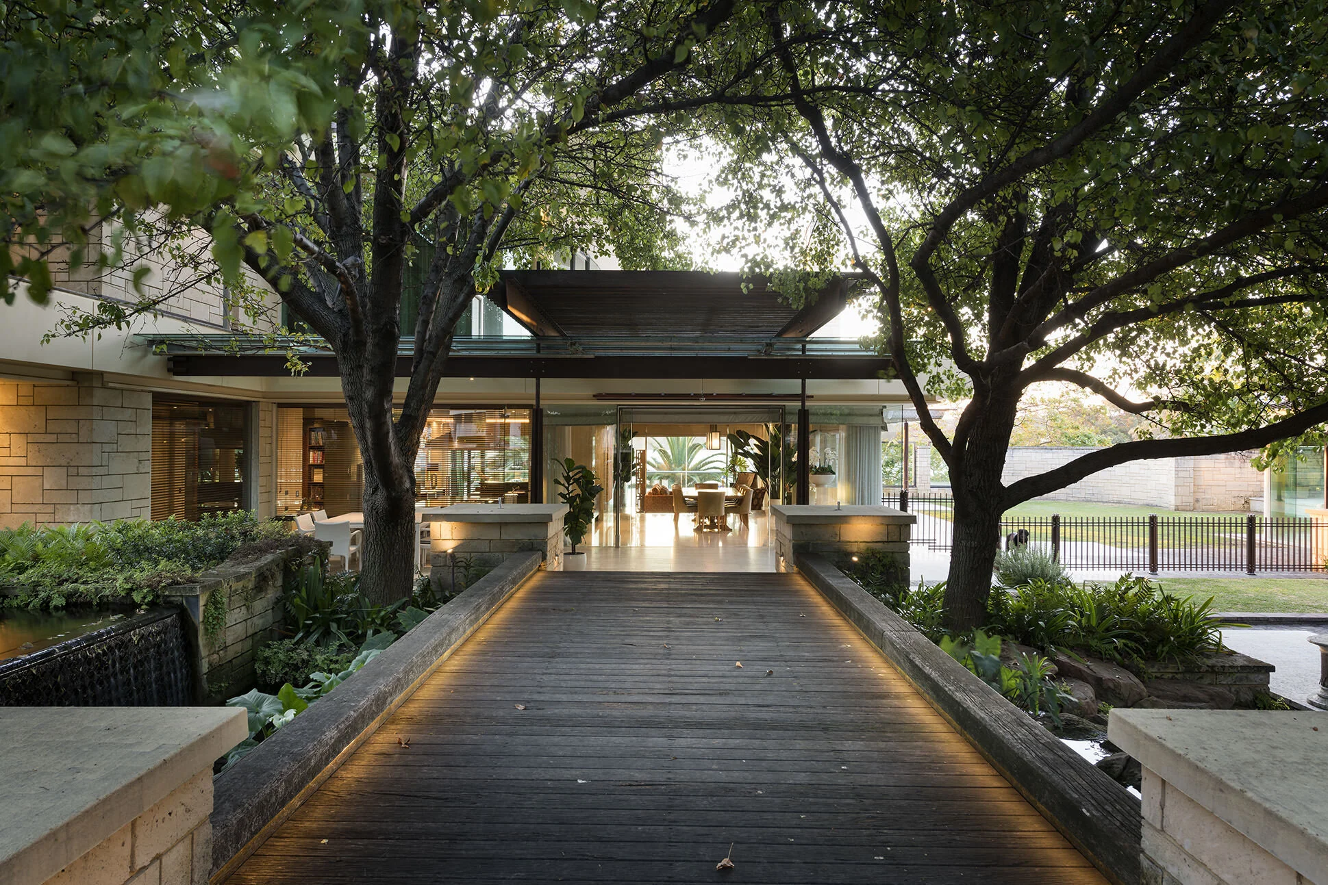 Landscaped garden approach to Watkins Residence featuring a timber boardwalk, mature trees and contemporary architecture, creating a welcoming arrival experience connected to nature.