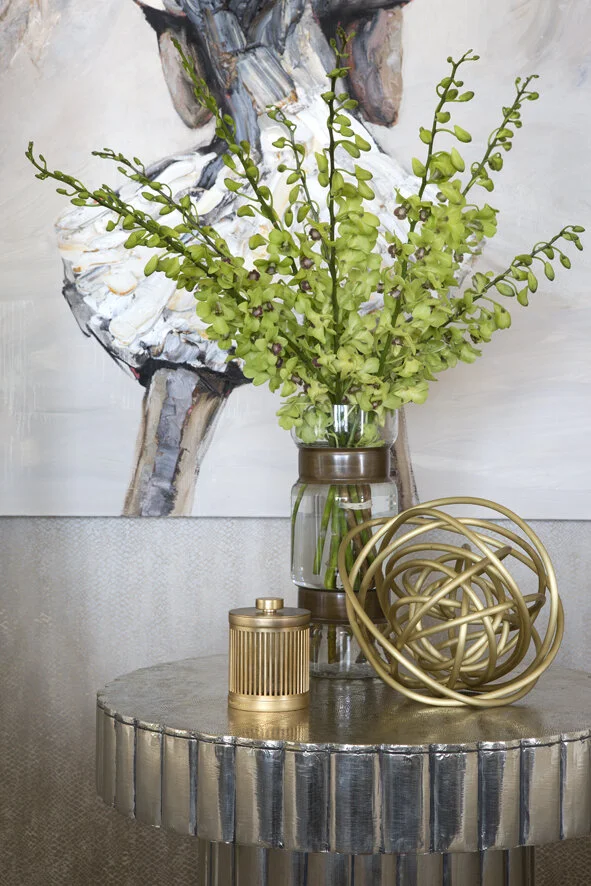 Styled console table vignette at Arabella Residence featuring a textured metallic side table, decorative sculptural accessories, fresh greenery and contemporary artwork, showcasing Luis La Pegna's layered approach to luxury interior styling.