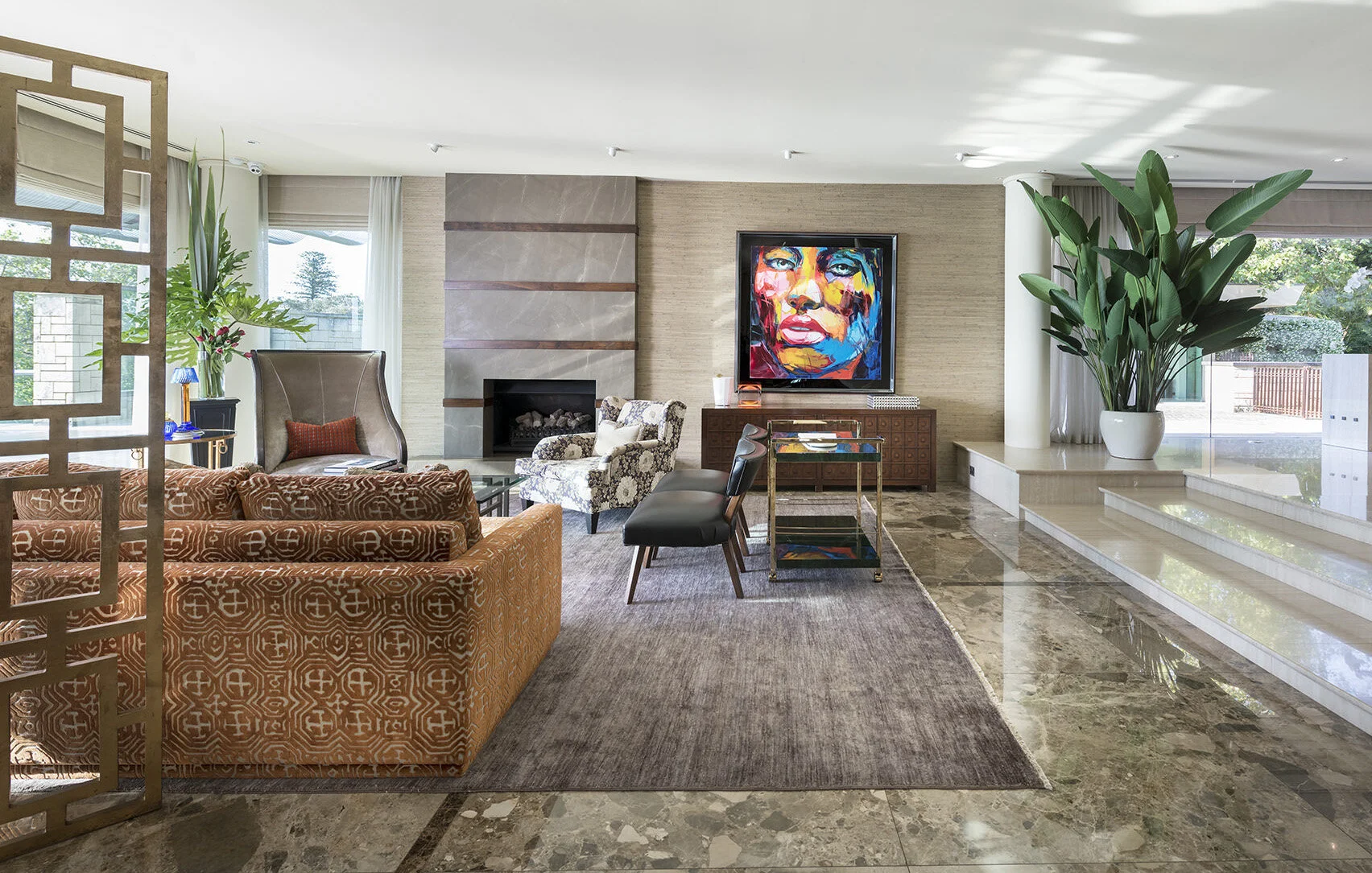Watkins Residence living room featuring layered seating, marble flooring, indoor plants, a fireplace, colourful artwork and contemporary residential interior styling.