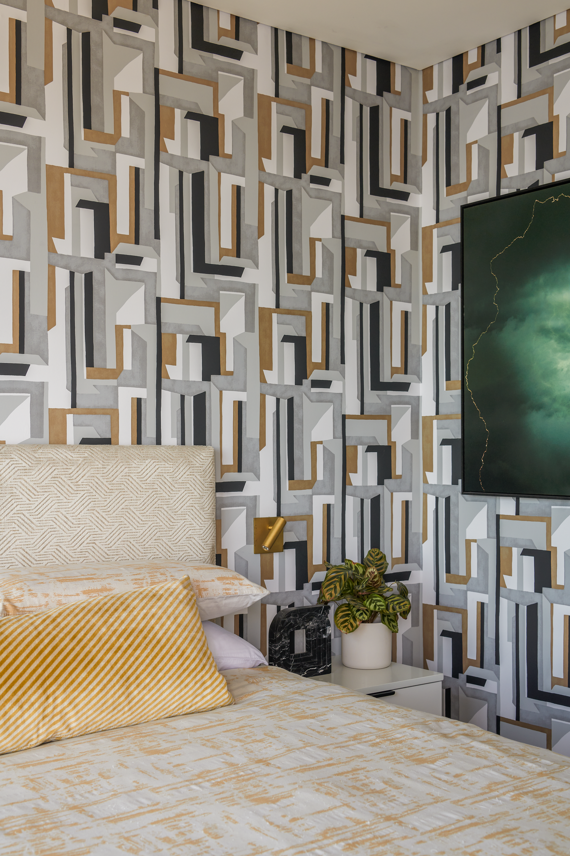 Contemporary bedroom featuring geometric statement wallpaper, layered neutral textiles and brushed brass accents. Custom upholstery, graphic patterns and curated styling create a sophisticated and luxurious retreat with modern character.