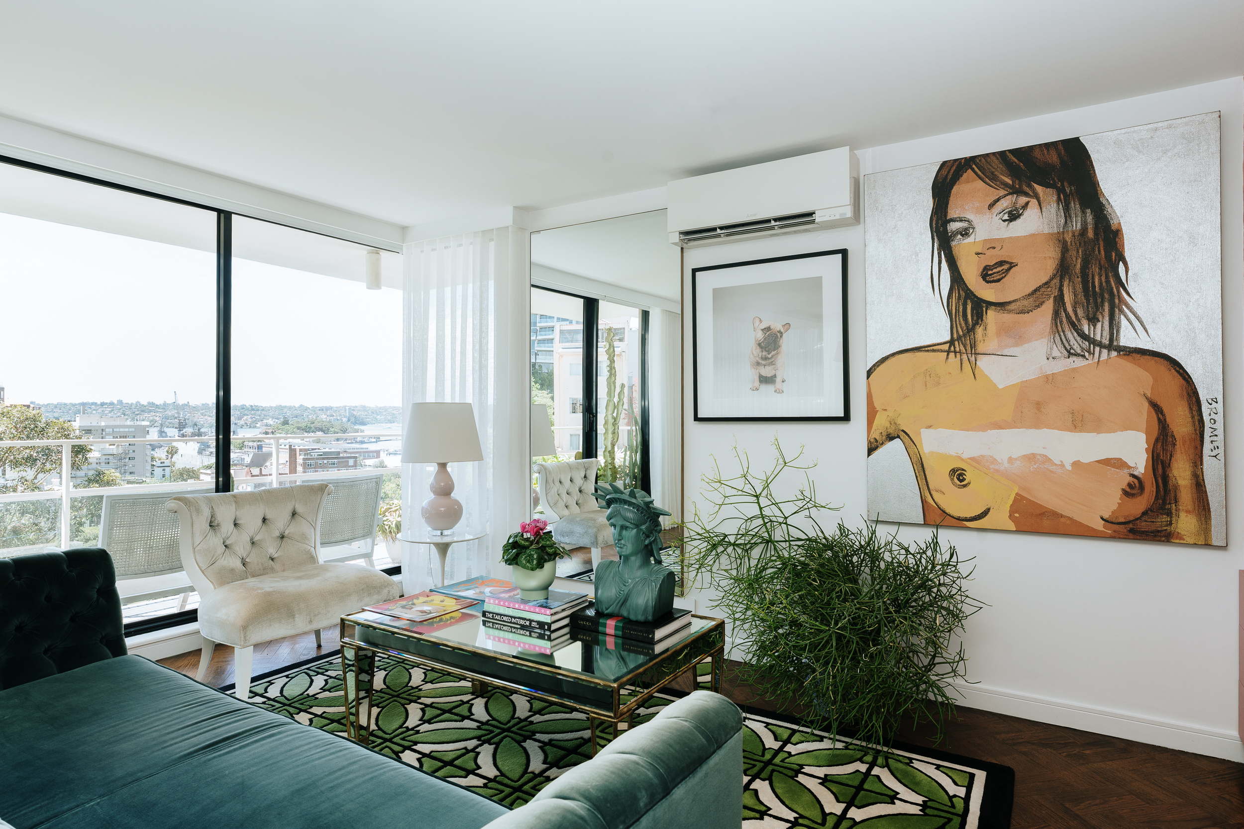 Living room with panoramic harbour views, floor-to-ceiling glazing and a curated collection of contemporary art. Teal velvet seating, statement furnishings, indoor greenery and layered textures create a vibrant yet sophisticated interior.