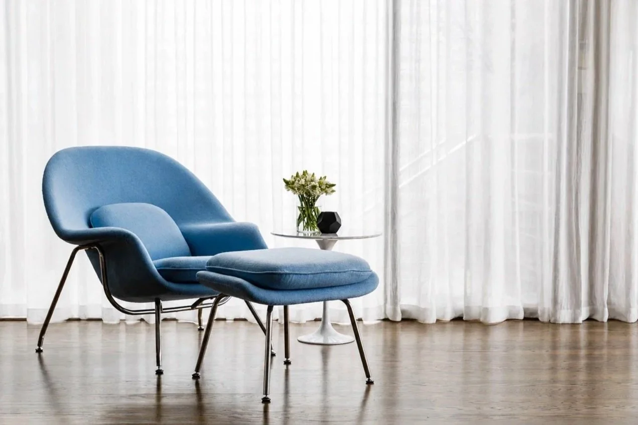 Mathieson Residence interior detail featuring a blue lounge chair and ottoman beside a small white side table, flowers and sheer curtains.