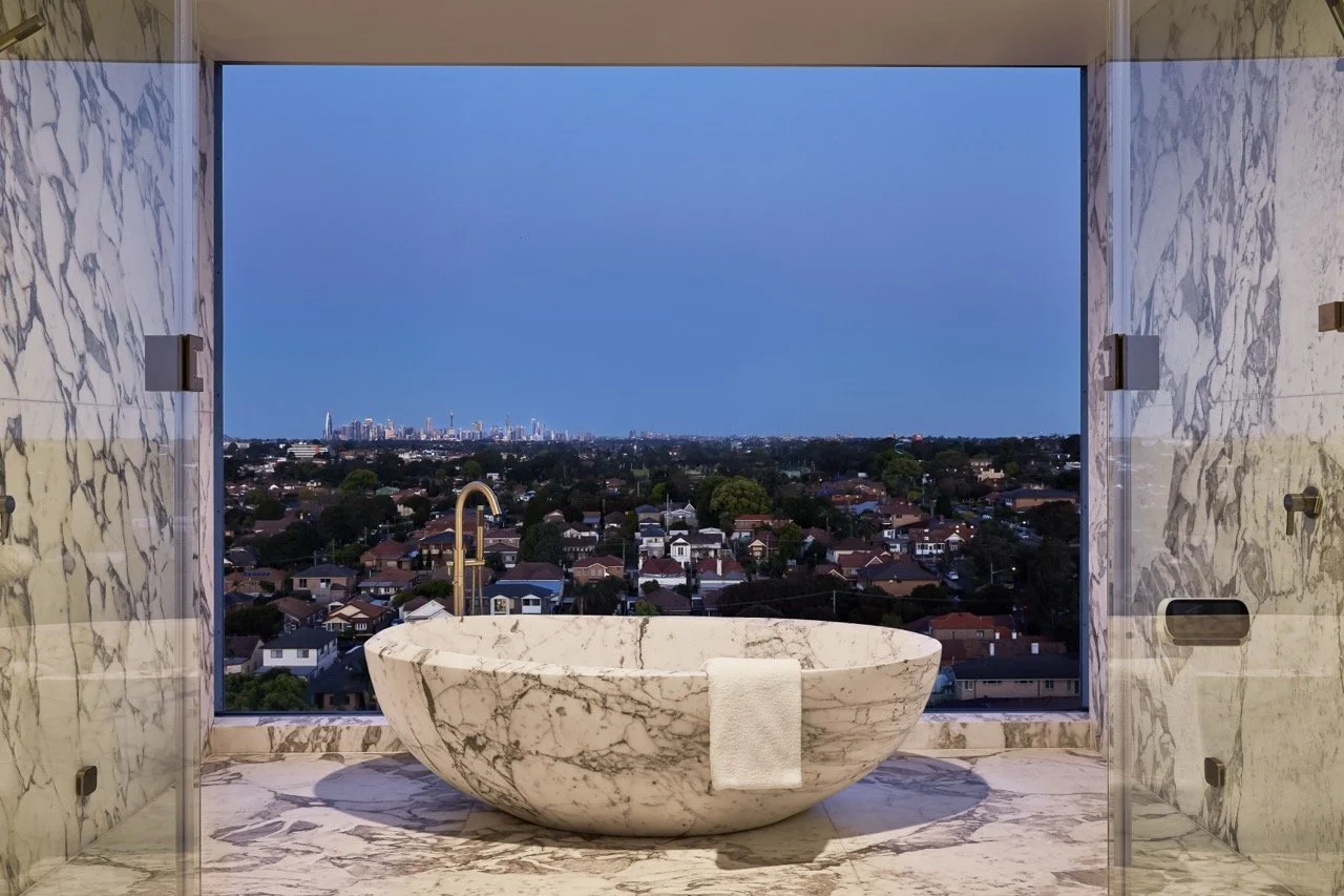 Burwood Residence marble bathroom featuring a freestanding stone bathtub, brass tapware, full-height marble walls and an expansive city view.