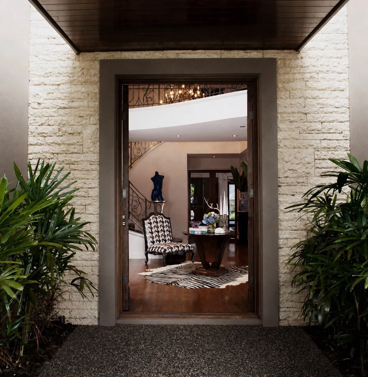 Kenmore Residence entryway with textured stone facade, timber-framed doorway, lush greenery and view into the styled foyer.