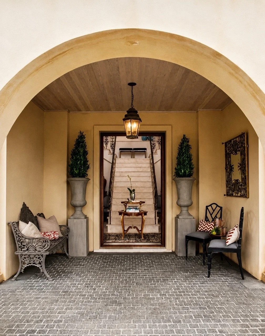 View Residence entry portico with arched doorway, patterned tile floor, decorative seating, potted topiary and traditional exterior detailing.