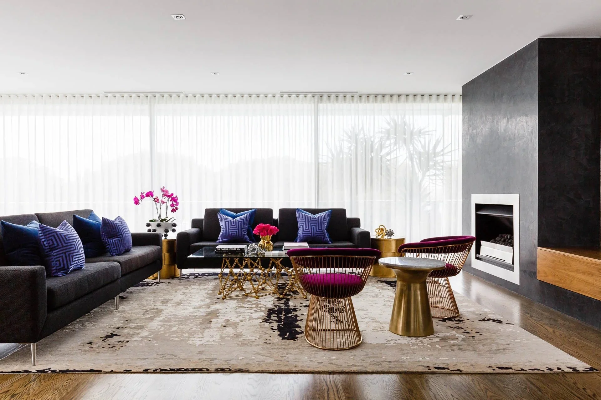 Luxury living room at Mathieson Residence featuring a sculptural black fireplace, charcoal sofas with cobalt blue cushions, brass furniture accents and contemporary residential interior styling by Luis La Pegna.