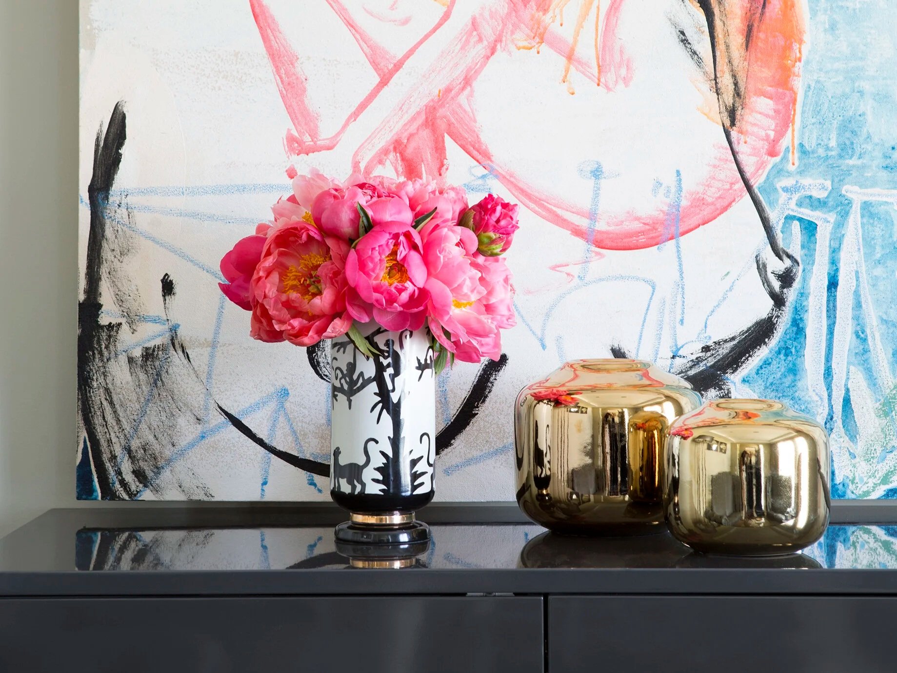 Styled console vignette at Carron Residence featuring fresh pink florals, metallic decorative vessels and contemporary artwork, creating a layered and elegant interior styling moment.