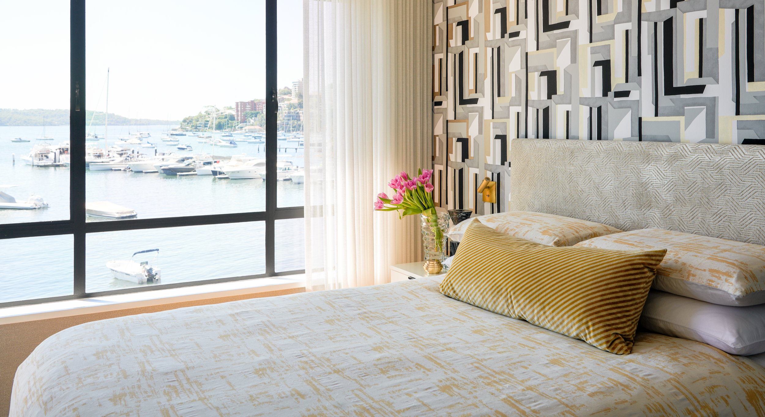 Luxury master bedroom at Stafford Residence overlooking the marina, with bespoke geometric wallcovering, tailored drapery, refined textures and soft natural light.