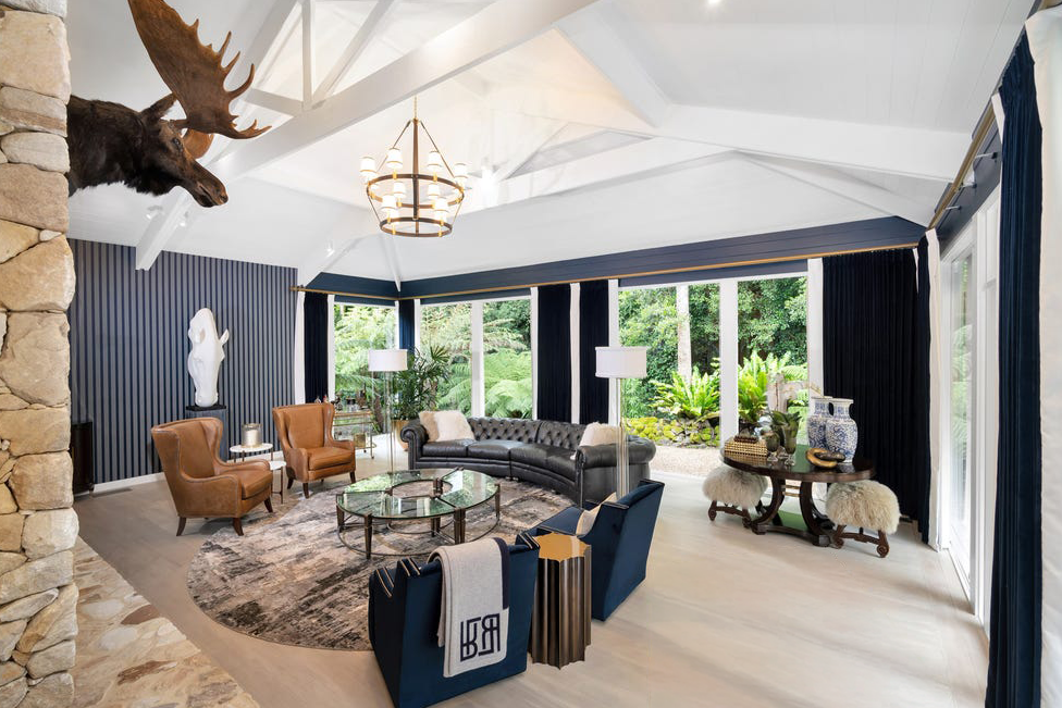 Luxury lounge at Pearsons Residence featuring vaulted ceilings, custom furnishings, navy accents, leather armchairs and floor-to-ceiling windows overlooking landscaped gardens.