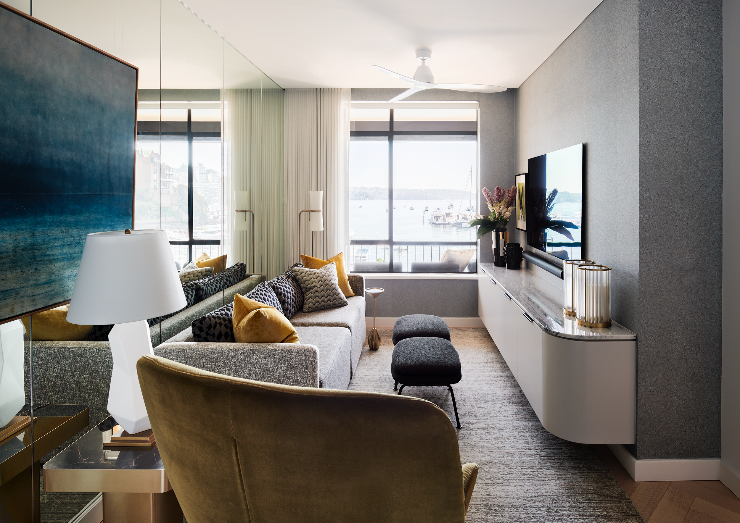 Contemporary waterfront living room featuring custom joinery, textured finishes and floor-to-ceiling harbour views. Layered neutral furnishings, sculptural lighting and refined detailing create a sophisticated, luxury apartment interior.