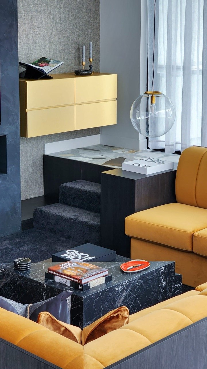 Wolli Residence living room with mustard sofa, dark marble coffee table, layered accessories and contemporary interior styling.