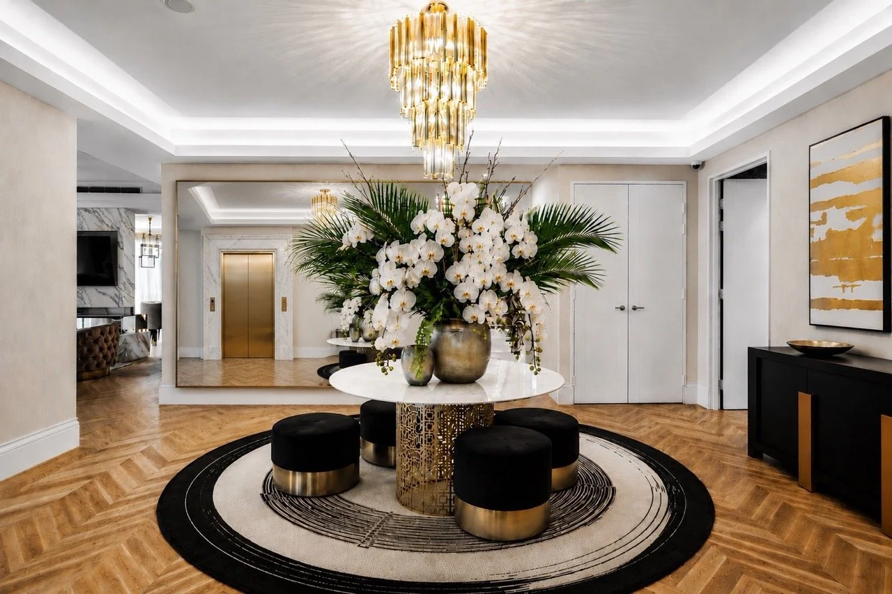 The Greens Penthouse entry foyer featuring a round marble table with oversized white orchid arrangement, gold chandelier, black and cream circular rug, herringbone timber flooring and contemporary luxury finishes.