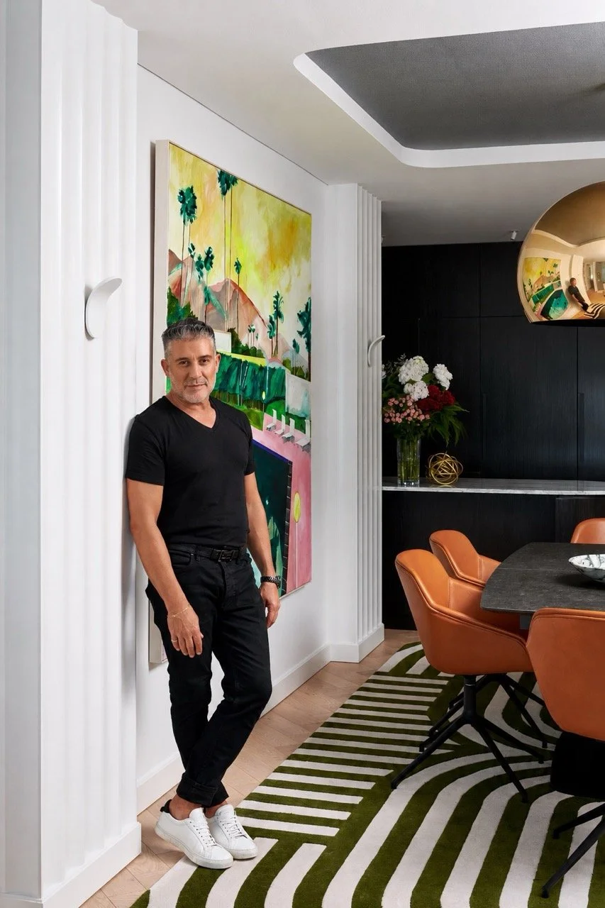 Luis La Pegna standing in a contemporary dining room beside colourful artwork, fluted white wall panels and tan leather chairs.