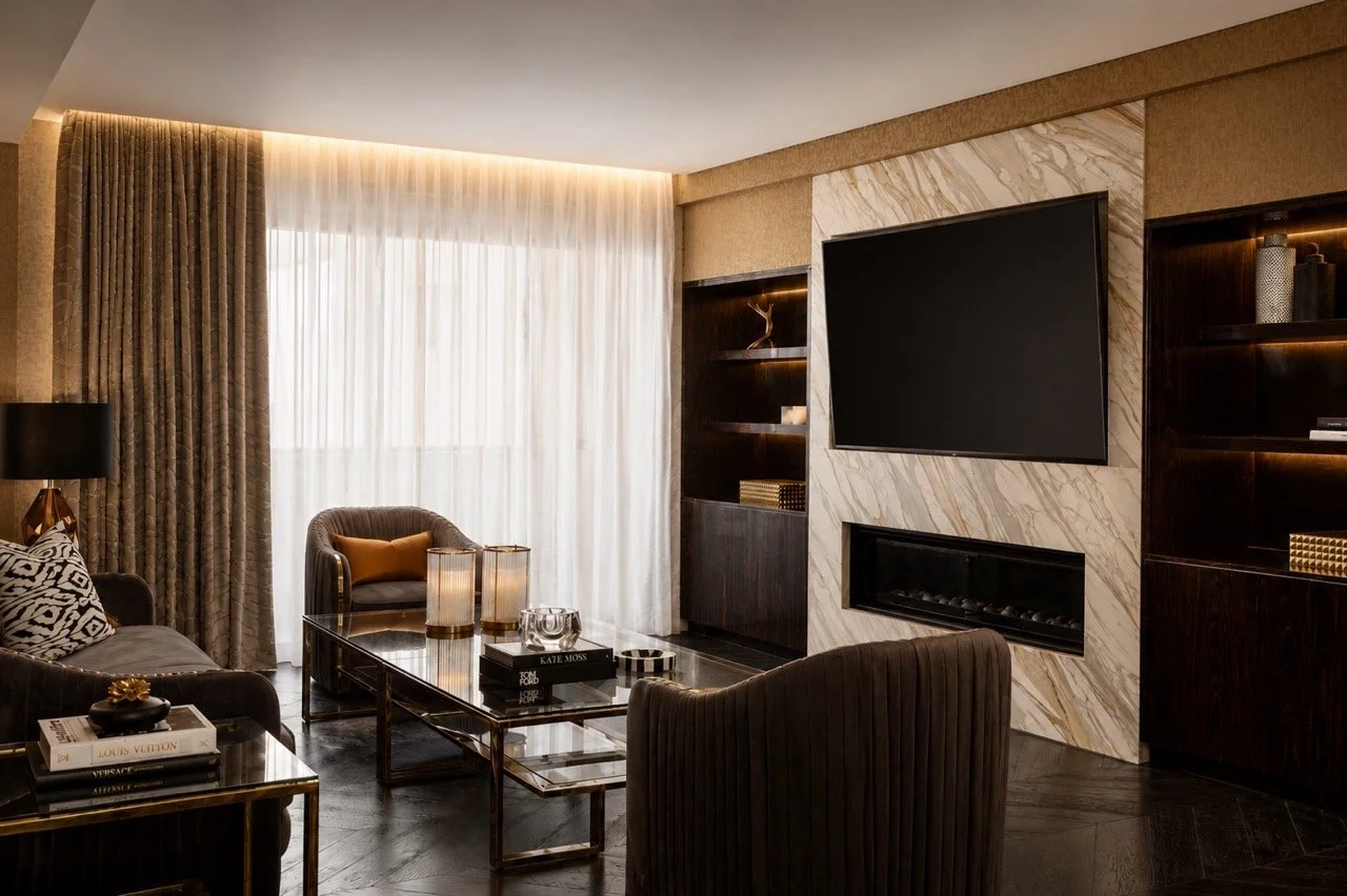 Burwood Penthouse lounge featuring a marble fireplace wall with mounted TV, dark timber joinery, layered seating, sheer curtains and warm contemporary lighting.