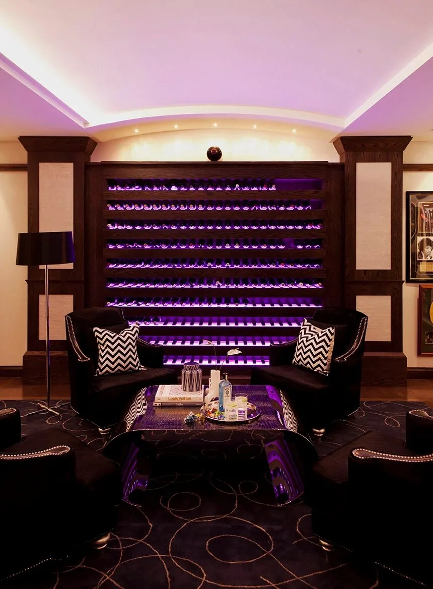 Kenmore Residence wine lounge featuring illuminated wine storage, dark seating, patterned flooring, mirrored details and purple accent lighting.