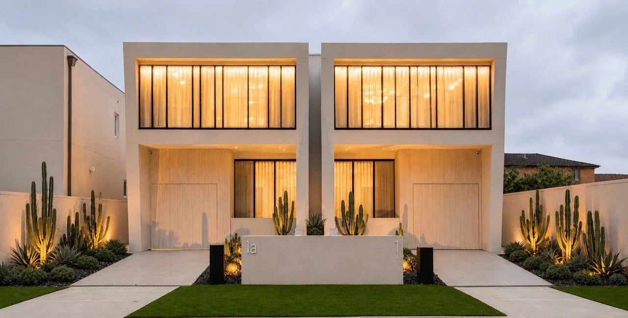Modern two-storey residence with a sculptural white facade, floor-to-ceiling glazing, architectural lighting and drought-tolerant landscaping at Wolli Residence, Sydney.