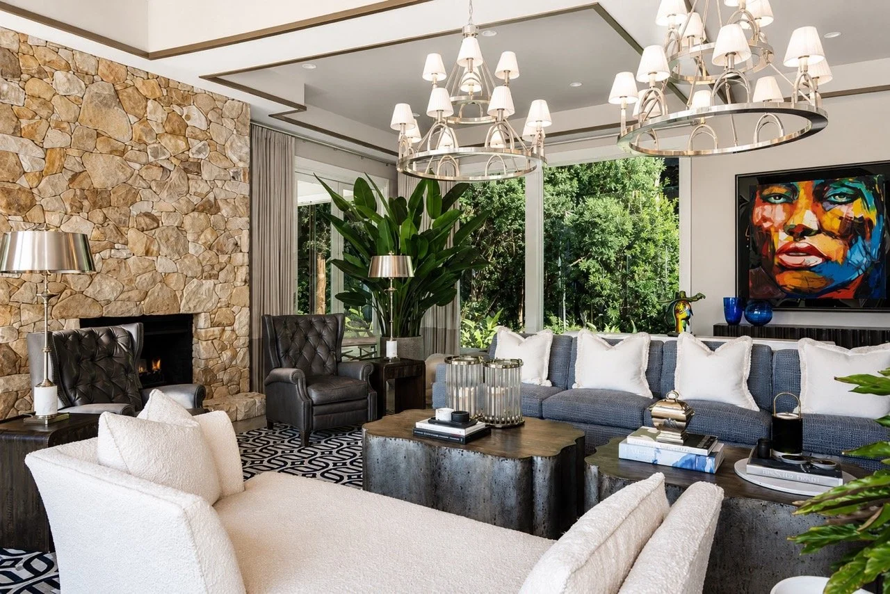 Luxury living room at Pearsons Residence in Robertson, NSW, featuring a floor-to-ceiling stone fireplace, custom furnishings, statement chandeliers, contemporary artwork, and large windows overlooking landscaped gardens.