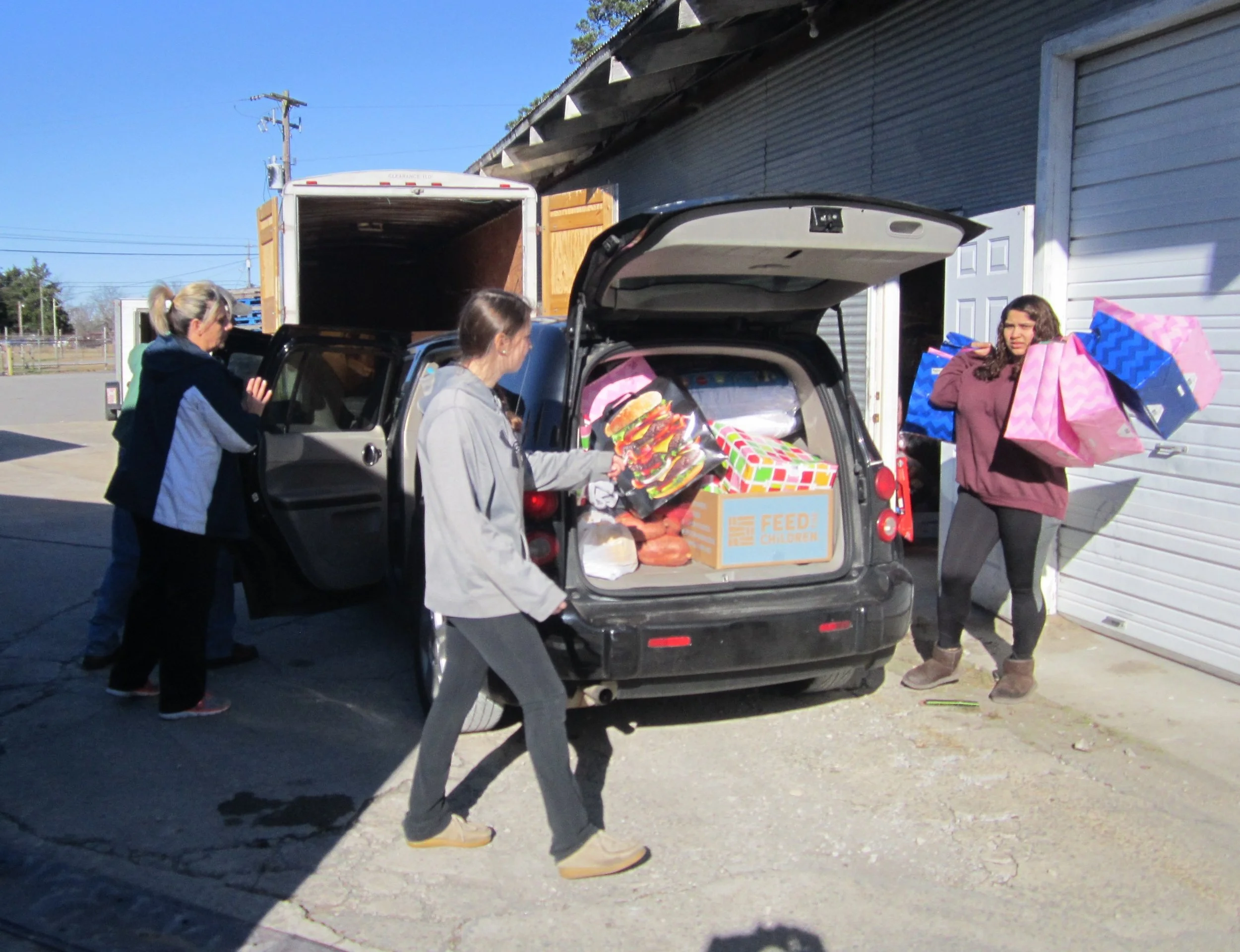 Volunteers help load cars with bags of Christmas gifts and donated groceries. Photo by Vicki Kennedy.