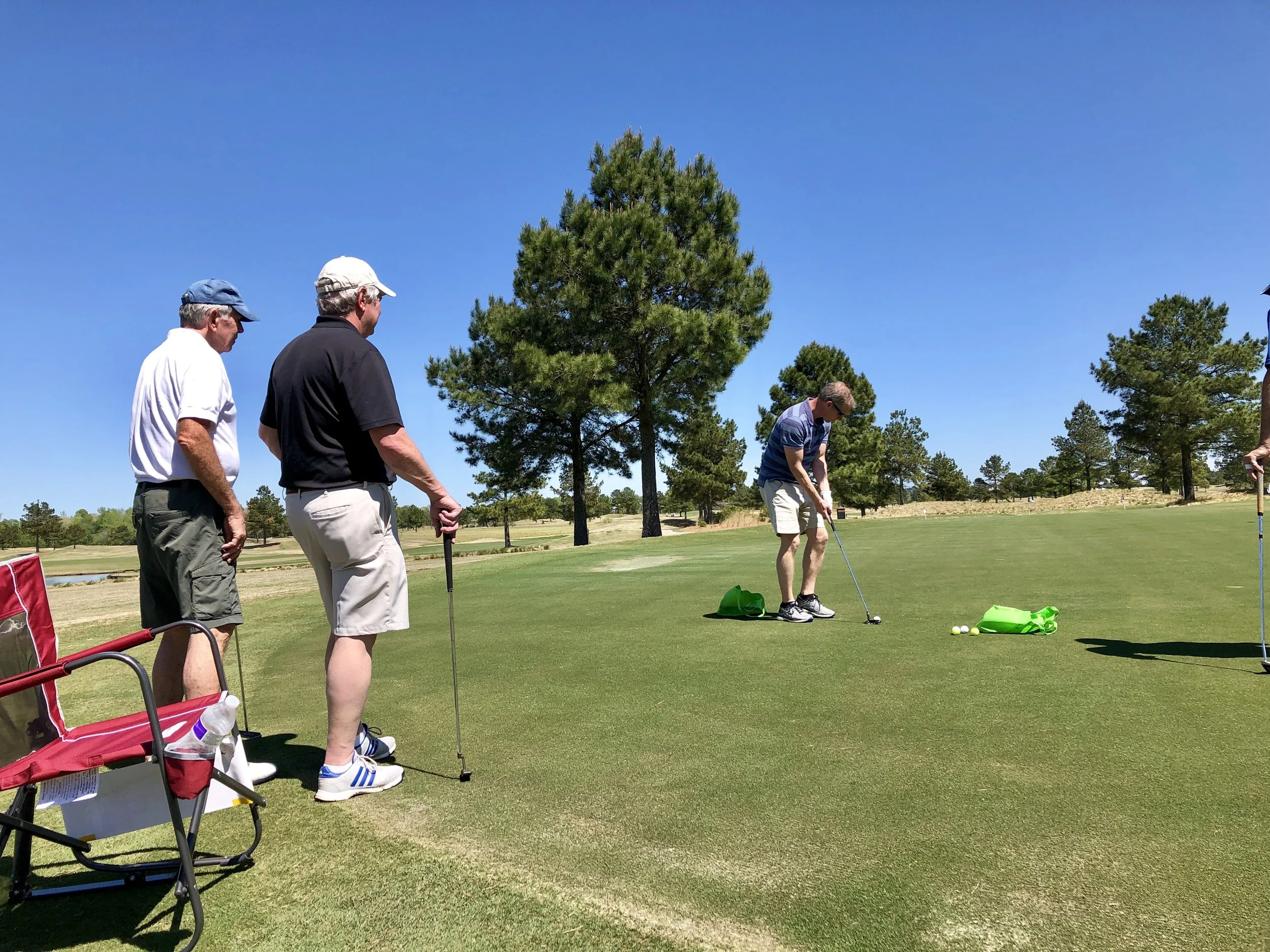 Jason McKnight lines up his putt in the putting contest during the tournament. Teammates Doug Hampton, Lee Trevino and Steve Katkaveck look on. Photo by Catherine Hardee / Neuse News