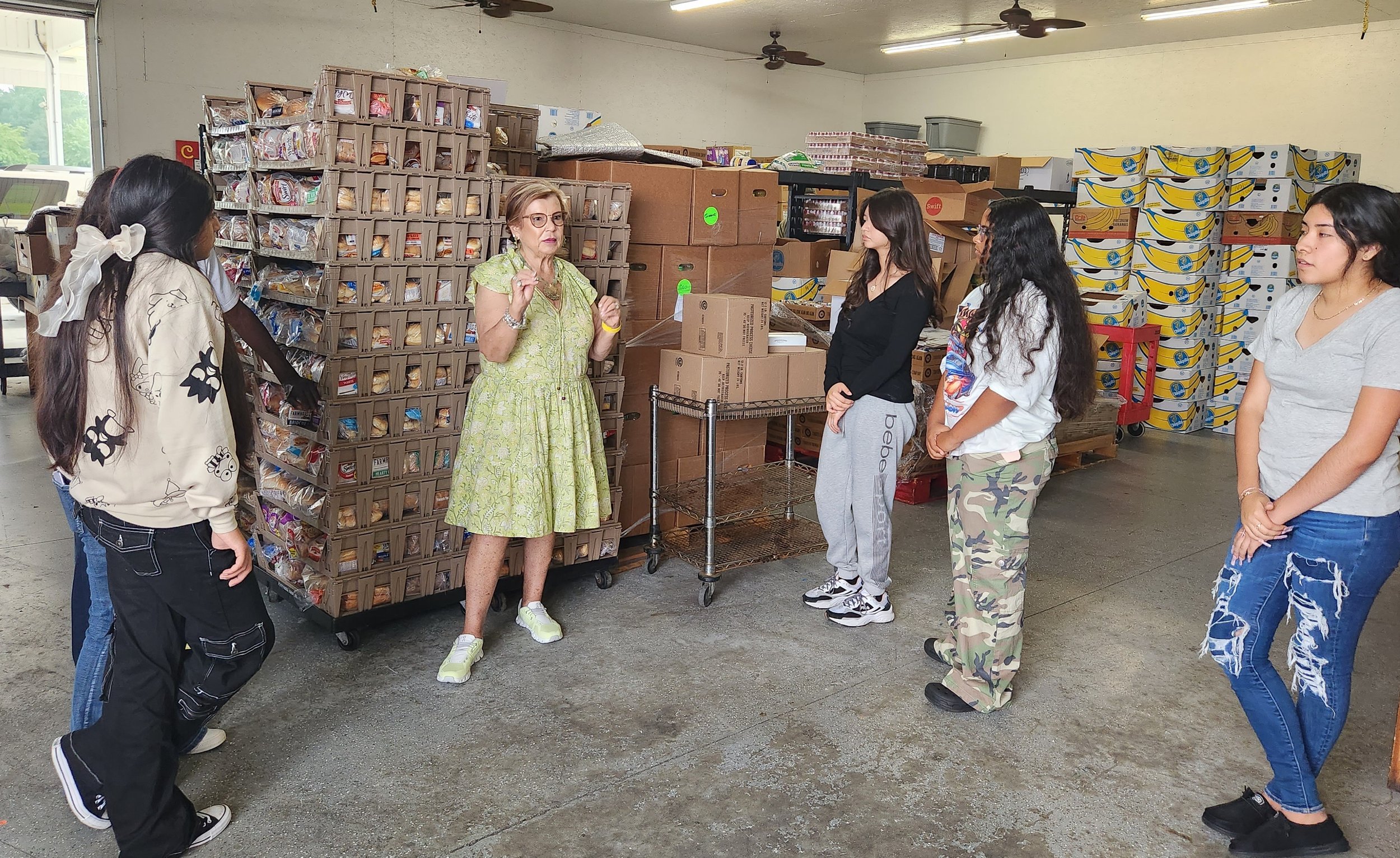  Amid the food ready to be packed and distributed, Executive Director(center), Dianne Andrews, educated GEC students about the work of Interfaith. 