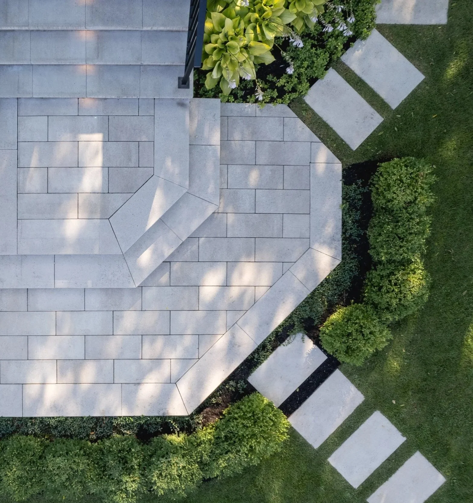 Vue aérienne d'une maison avec un toit en pierre, entourée de végétation et d'un chemin de pas en pierre.