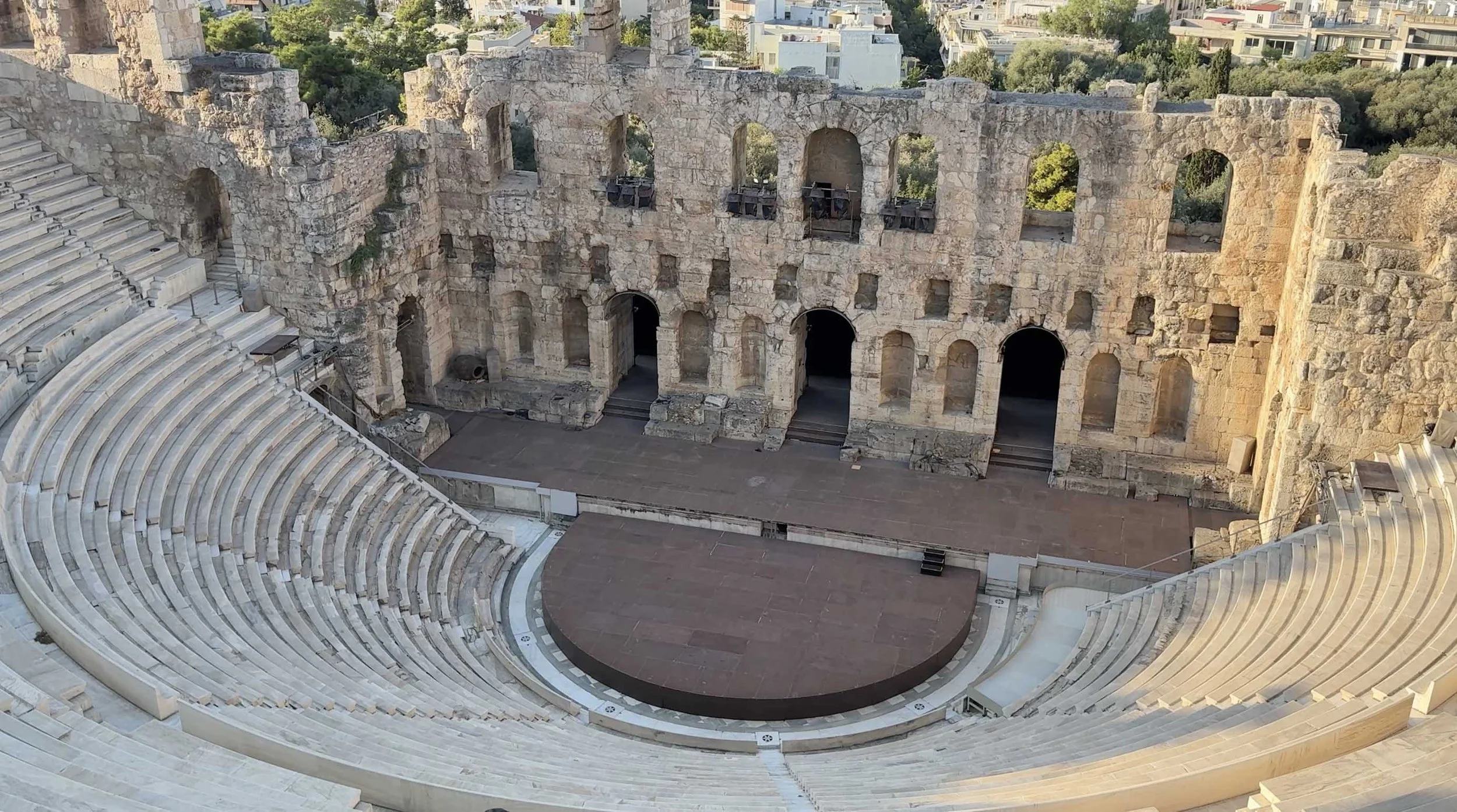 Ancient theater in Athens, Greece, with curved stone seating and an arched stone stage backdrop.