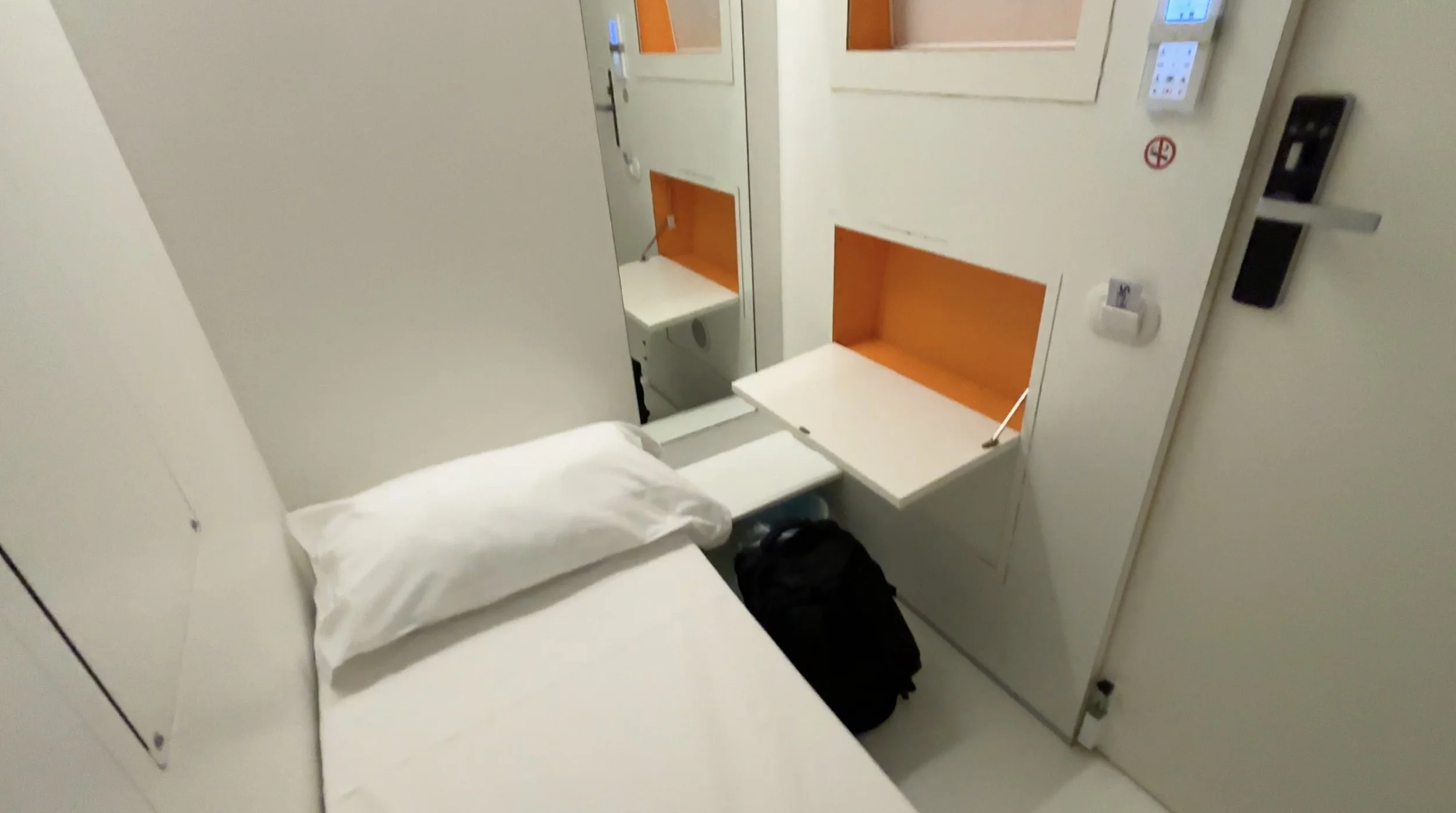 Bed, fold-down desk, mirror, and backpack inside a compact Benbo Capsule Hotel room in Naples.