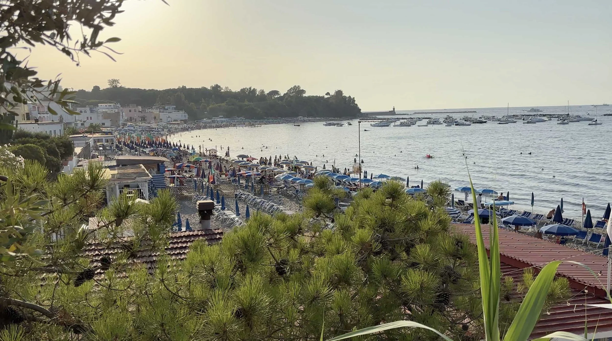 Beach at Lido Raggio di Luna in Ischia, Italy, with colorful umbrellas, sun loungers and swimmers in the bay.
