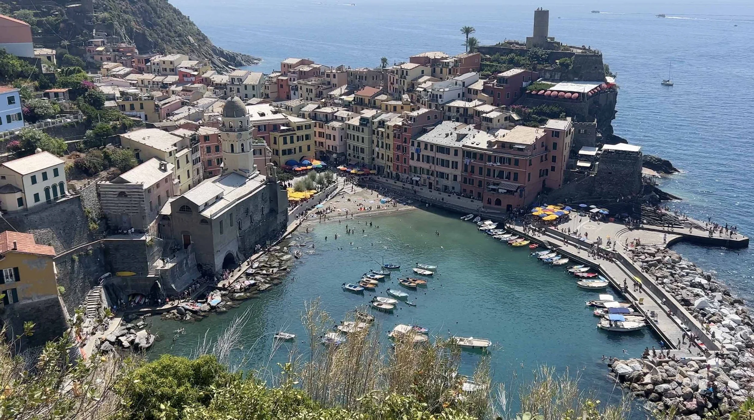 View over Vernazza’s harbor in Cinque Terre, Italy, with colorful waterfront buildings, small boats and a stone breakwater.