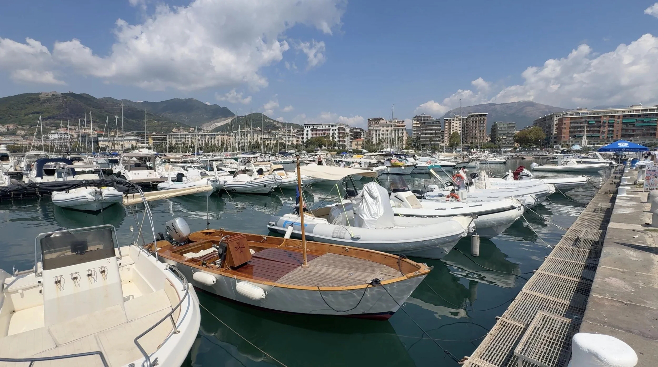 Boats moored in Salerno’s harbor in Italy, with waterfront buildings and mountains in the background.