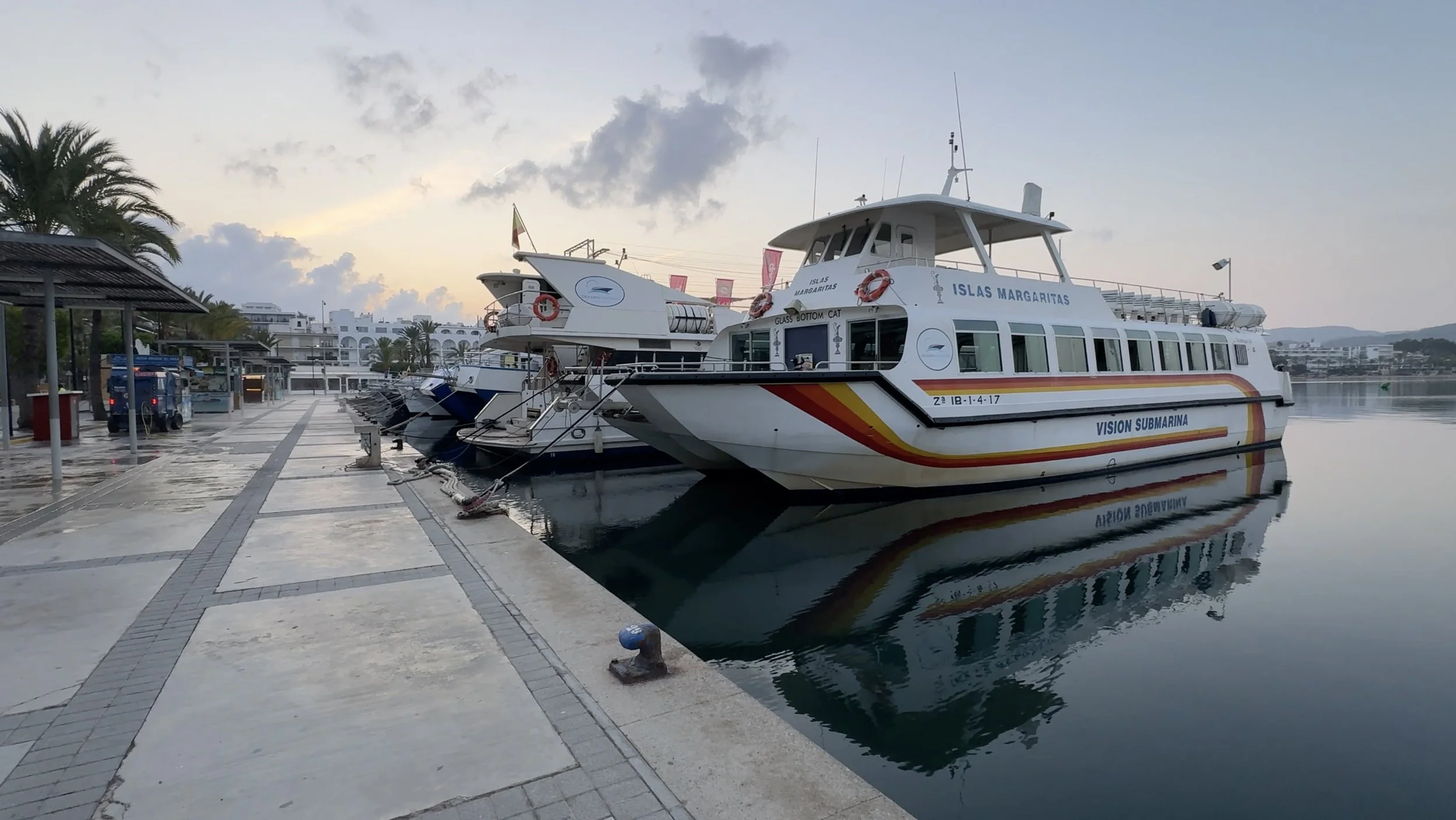 Tour boats reflected in calm water beside the promenade in Sant Antoni de Portmany, Ibiza.