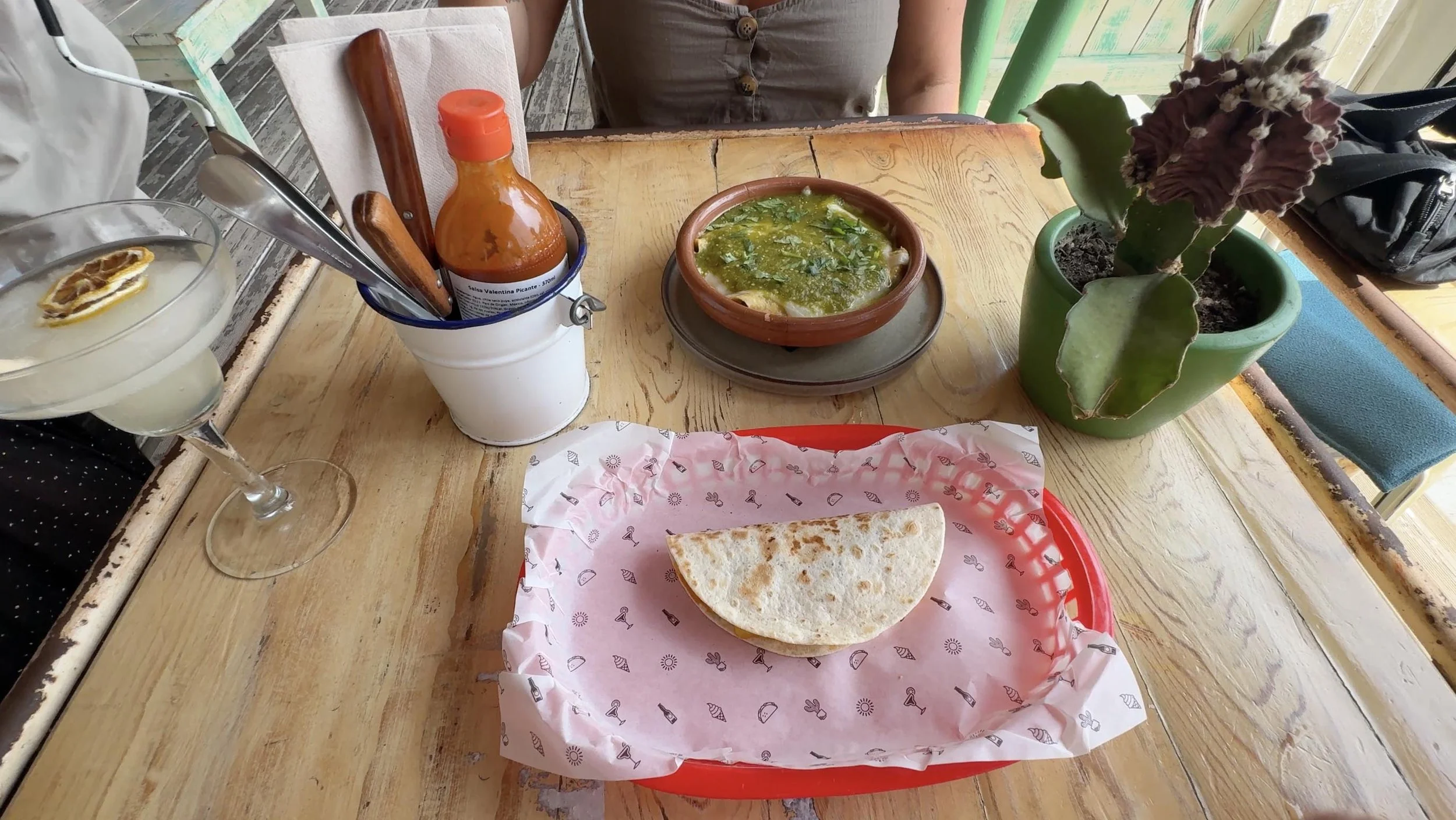 Mexican lunch in San Antonio, Ibiza, with a folded tortilla, green sauce, and a cocktail on a wooden table.