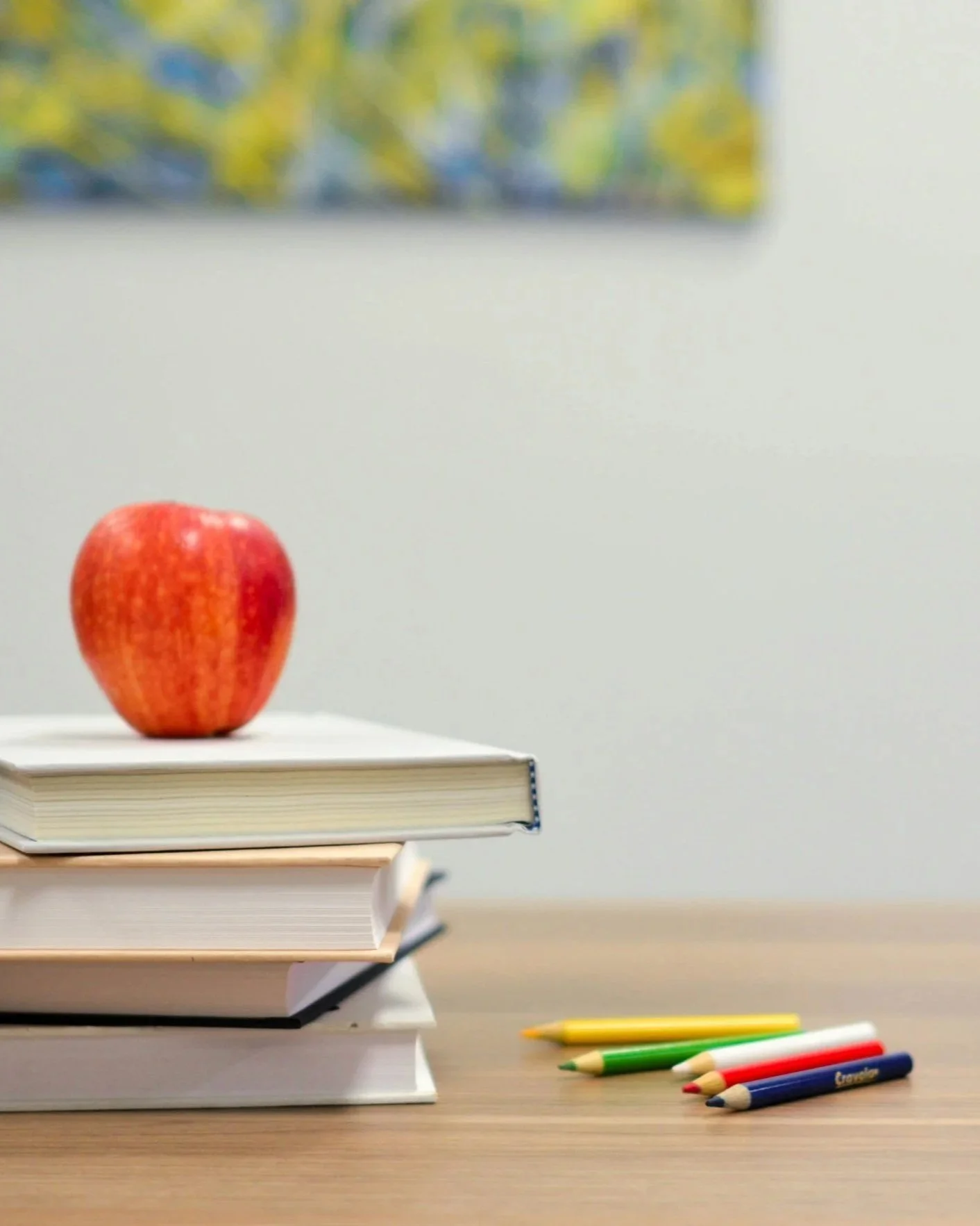 A honeycrisp apple sits atop a stack of books, next to some colored pencils