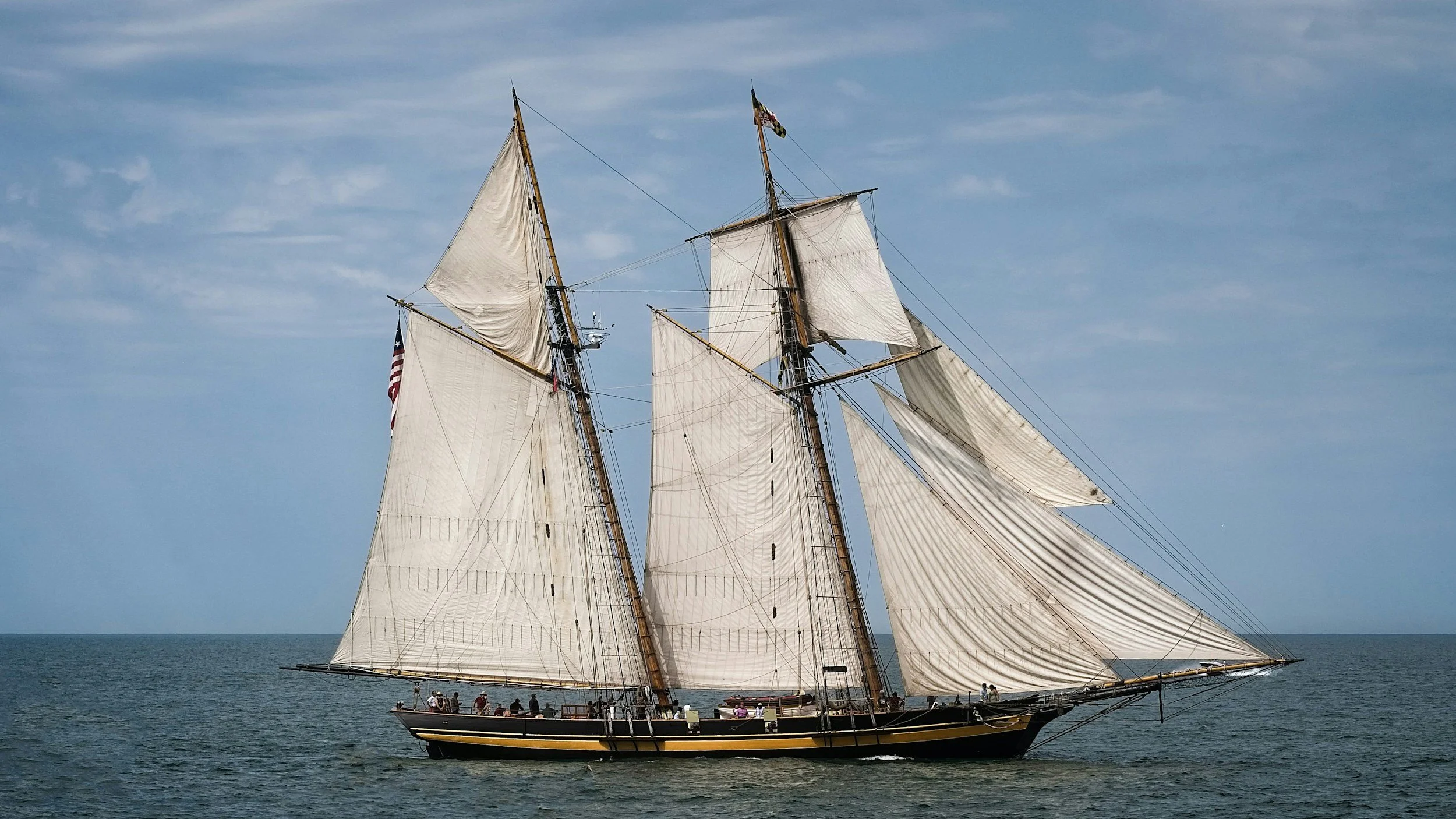 A squar-masted topsail schooner with 7 sails flying on a partly-cloudy day