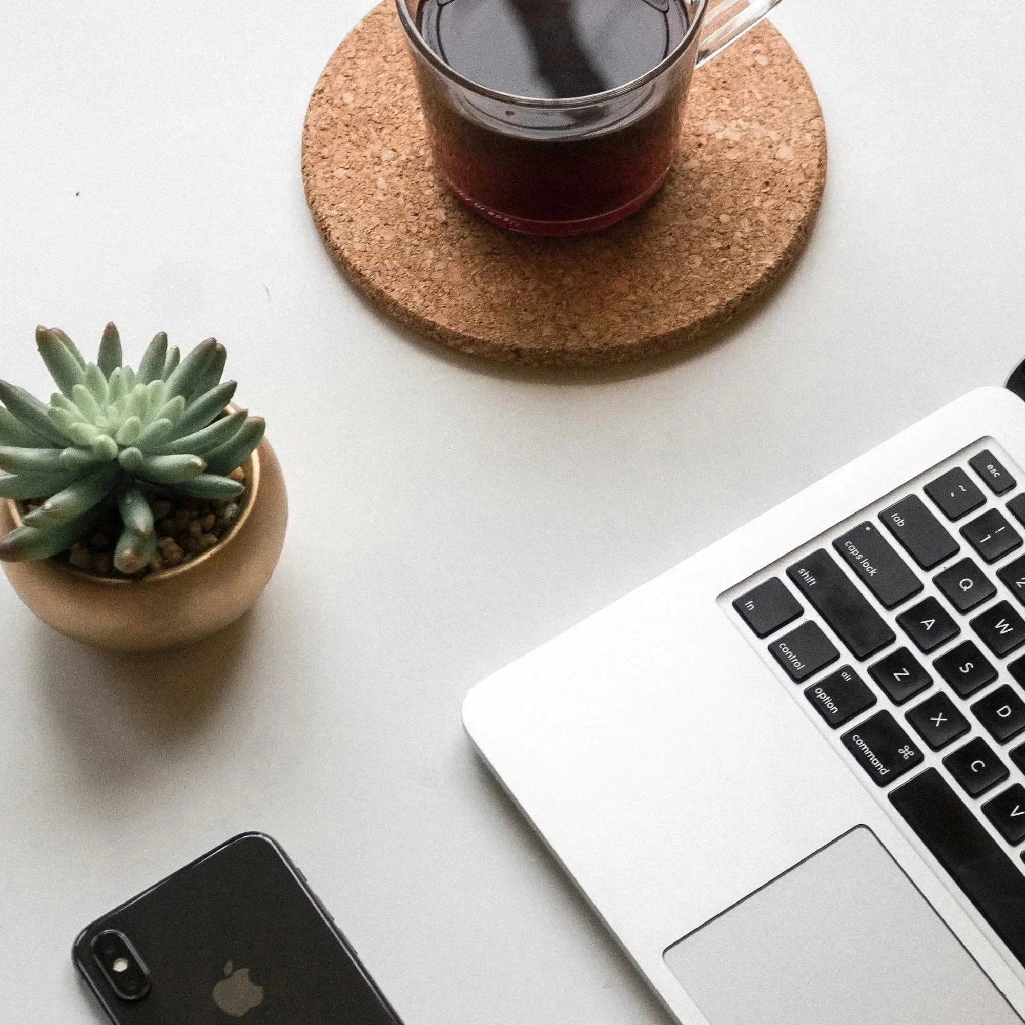 laptop, phone, succulent and black coffee arranged on a grey desk.