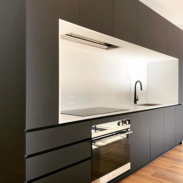 A compact kitchen with a strong contrast. 
The white composite stone benchtop, splashback and surrounds provide a practical bright working space. Monochromatic and timeless in style and palette, this kitchen is now ready for clients to introduce some