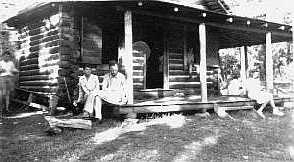 Cabin with porch. Man siting on porch is Mr. J. Brackin Kirkland.