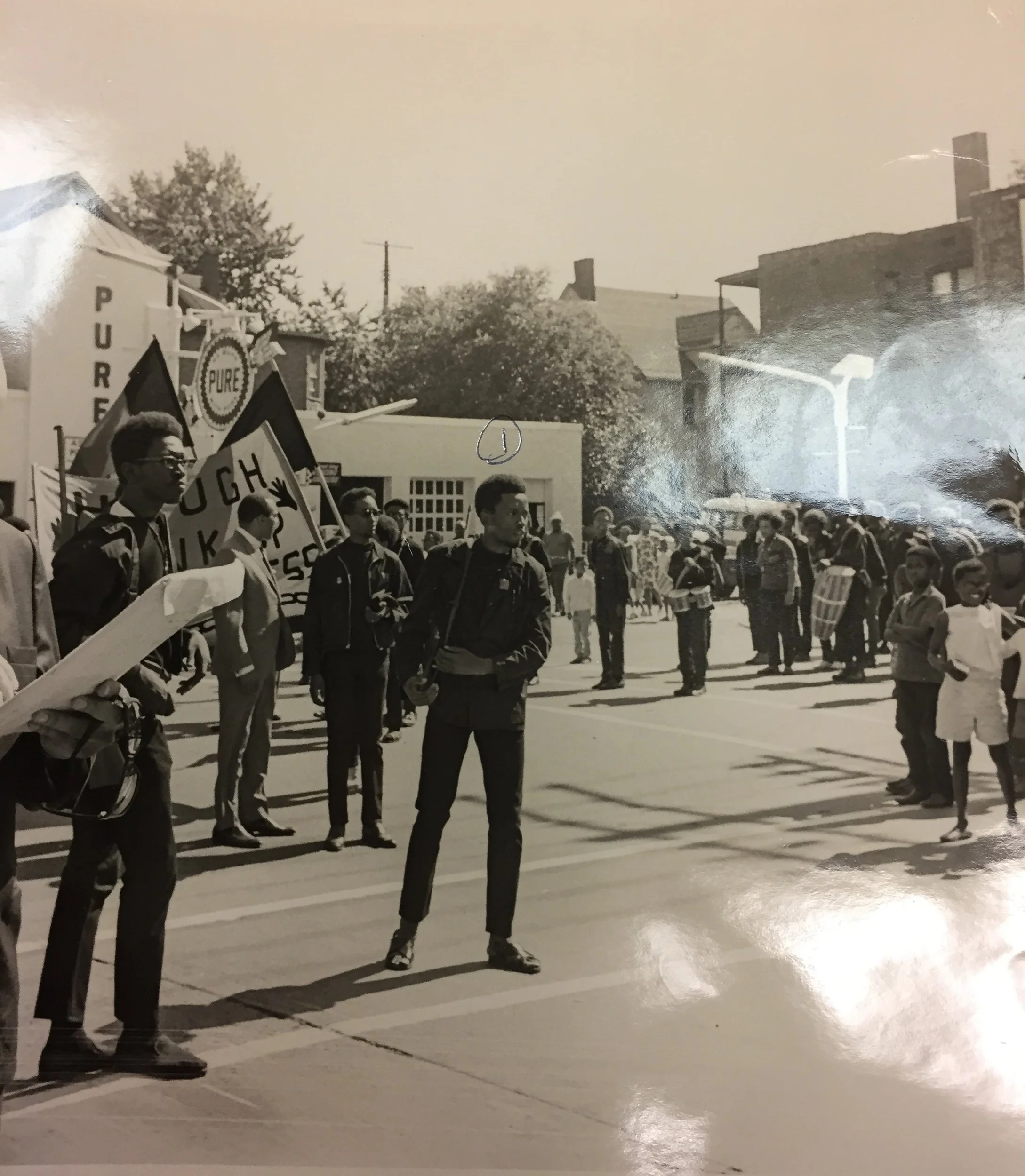 Police surveillance photo, Saturday, July 20, 1968, three days before the shootout. Mayor Carl Stokes in suit stands near Harllel Jones, leader of the Afro Set. The man in the center of the photo is Sababa Akili, a member of the Afro Set. Note the rifles. This is the kick-off of a parade commemorating the Hough Rebellion, which occurred two years earlier. Credit: Cleveland Police Museum