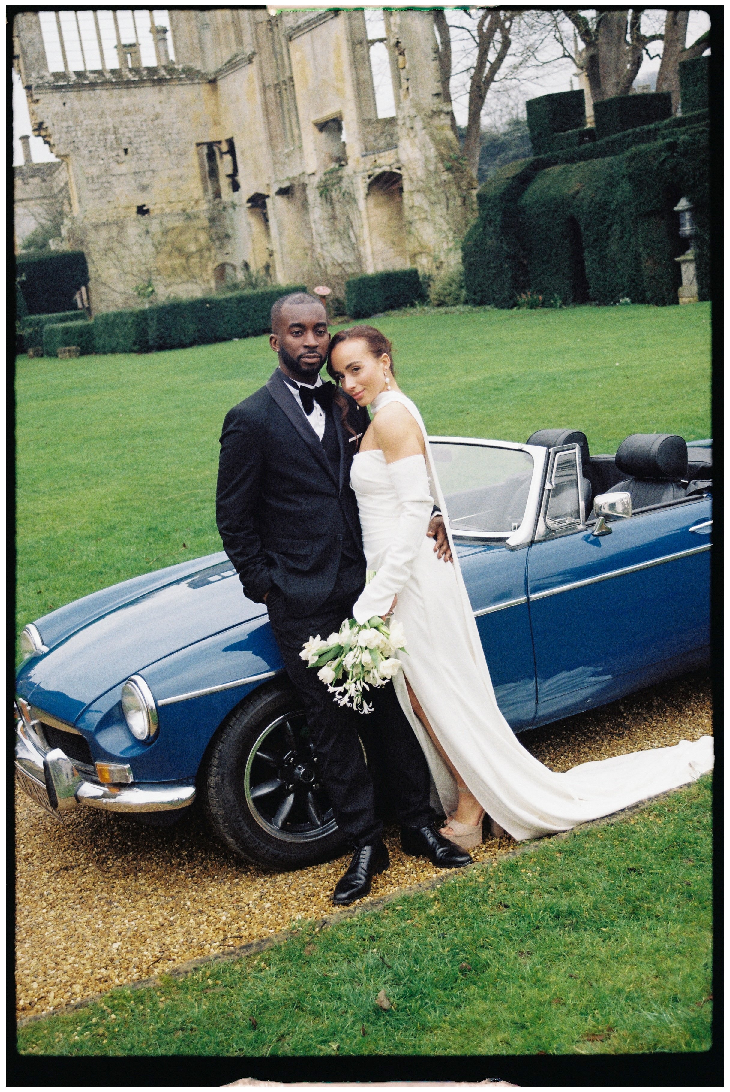 Bride and Groom standing in front of a classic car within the grounds of Sudeley Castle