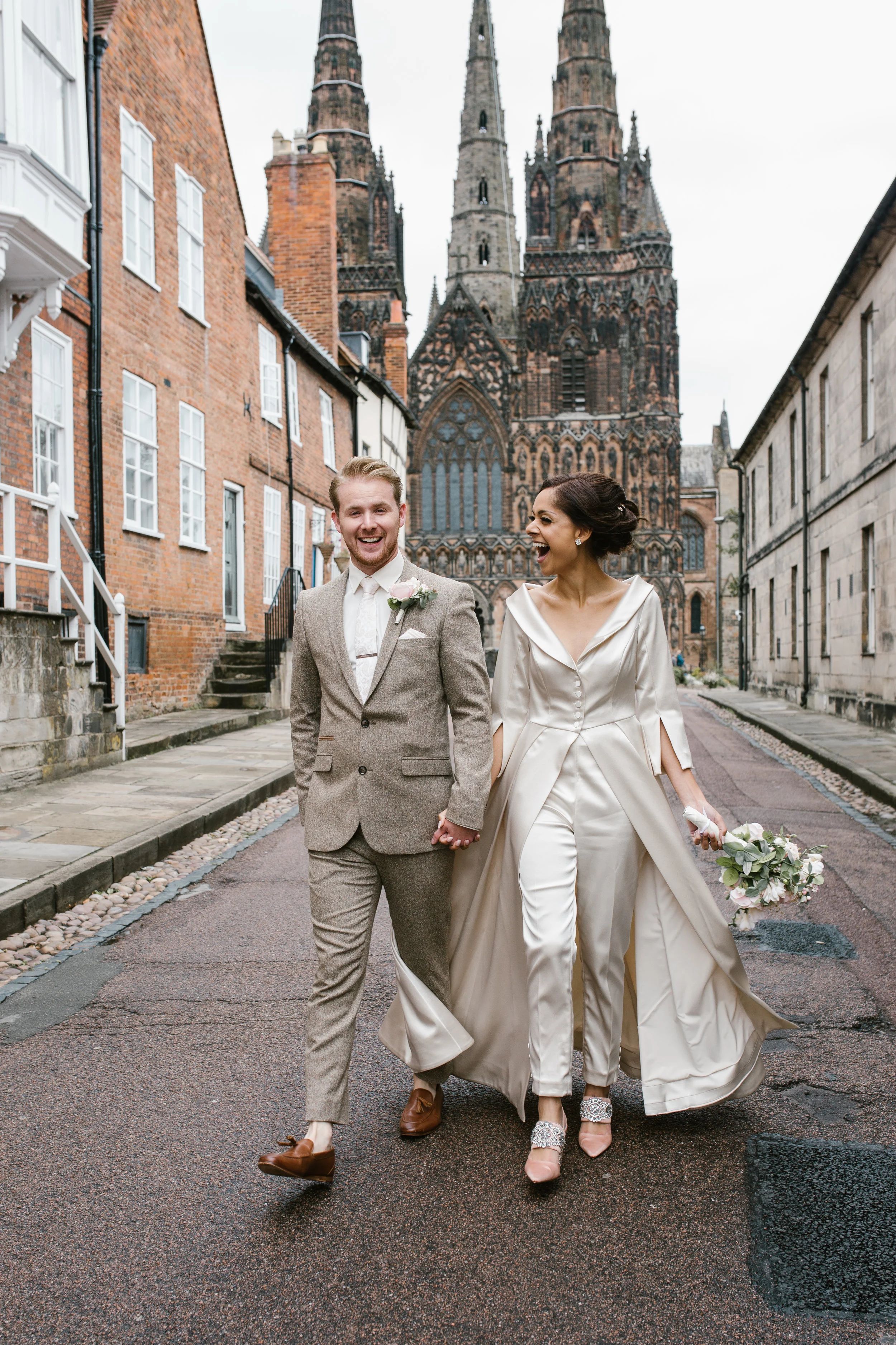 a very happy bride and groom walking holding hands laughing with lichfield cathedral in the background after their intimate ceremony- wedding photography in staffordshire