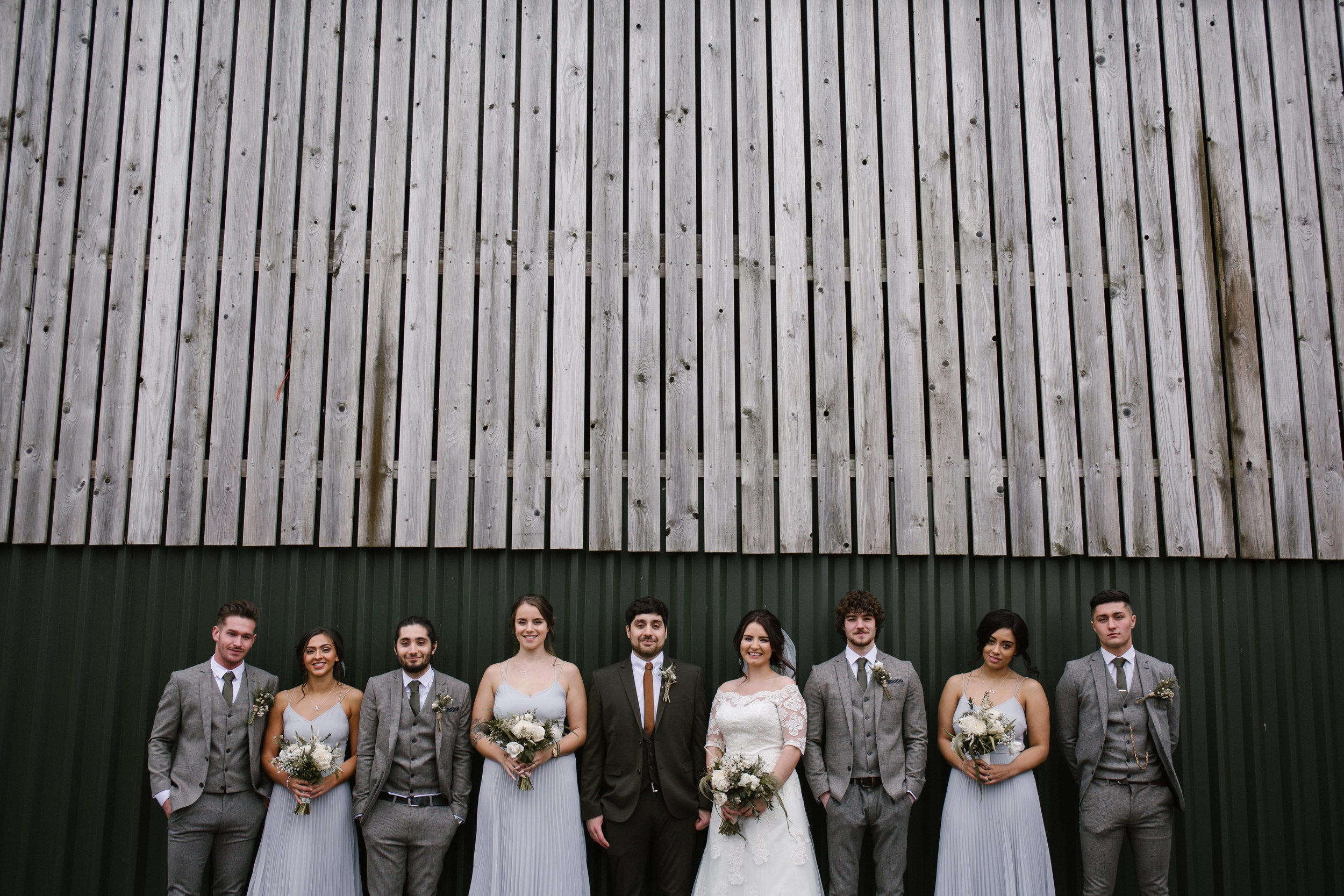 bridal party looking extra cool standing in front of a barn wall at sandhole oak barn in cheshire