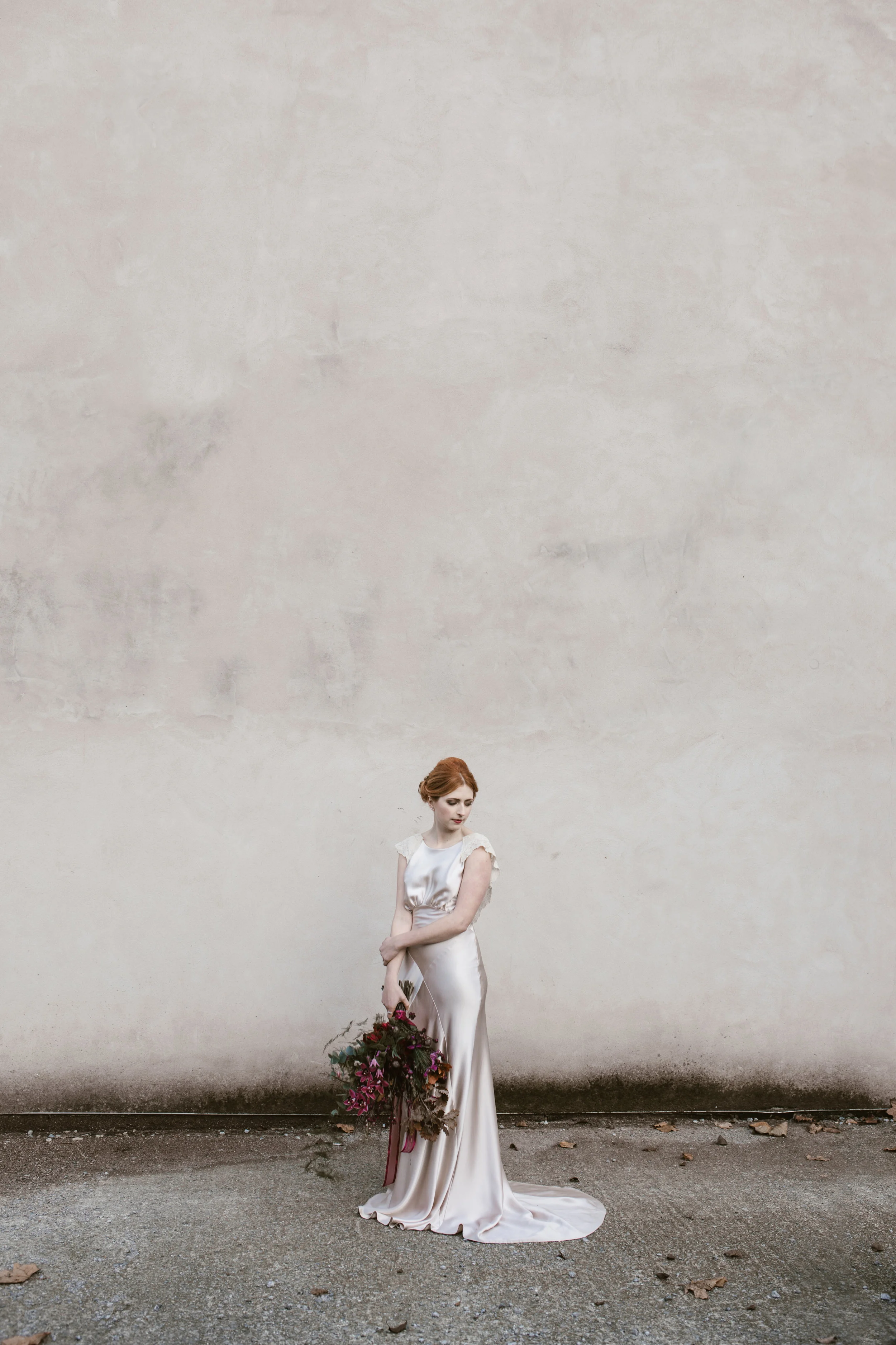 red headed bride stands against a concrete wall looking incredible holding red wild flowers