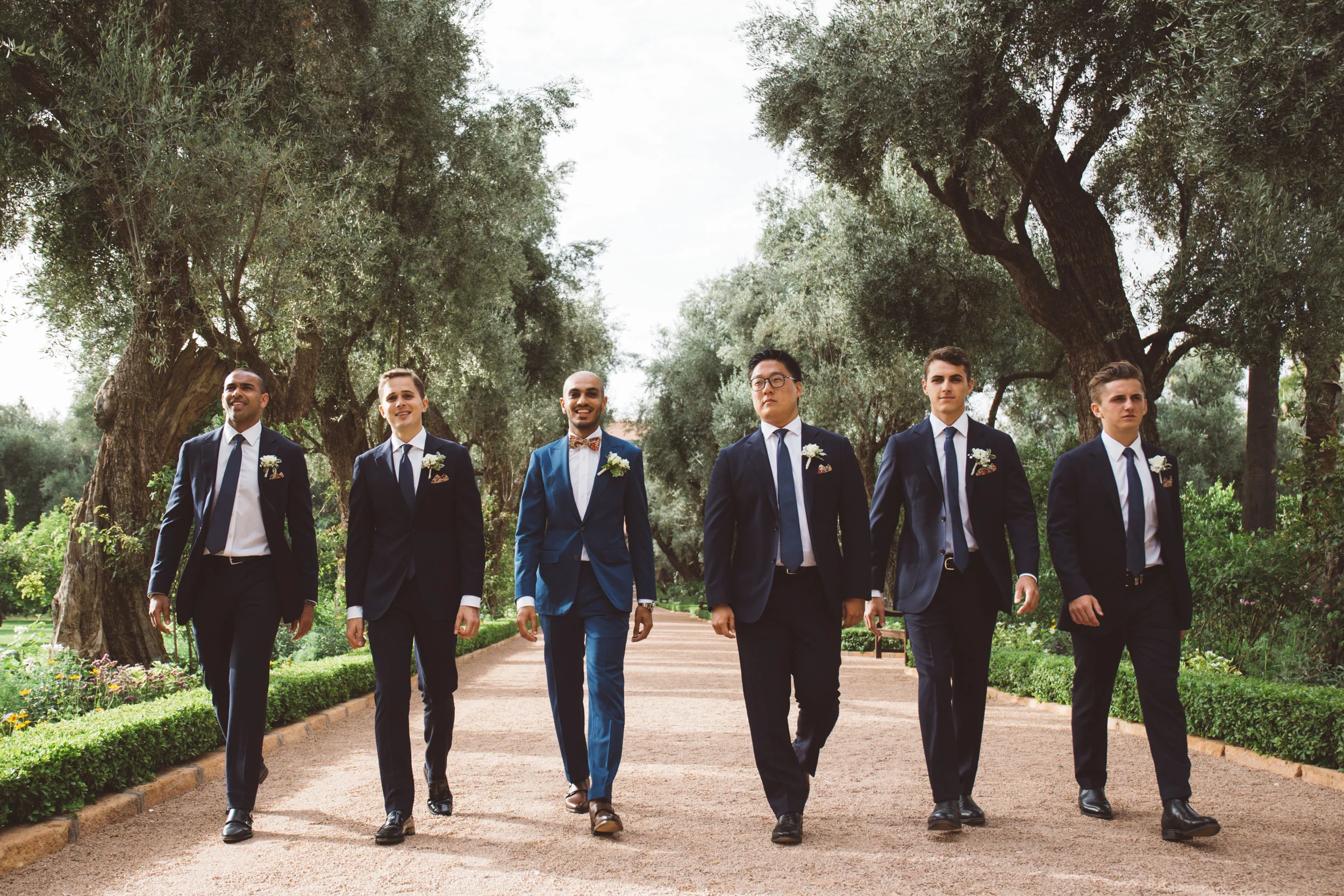 groomsmen all walk in a line towards the outdoor wedding ceremony at la mamounia hotel in marrakech morocco