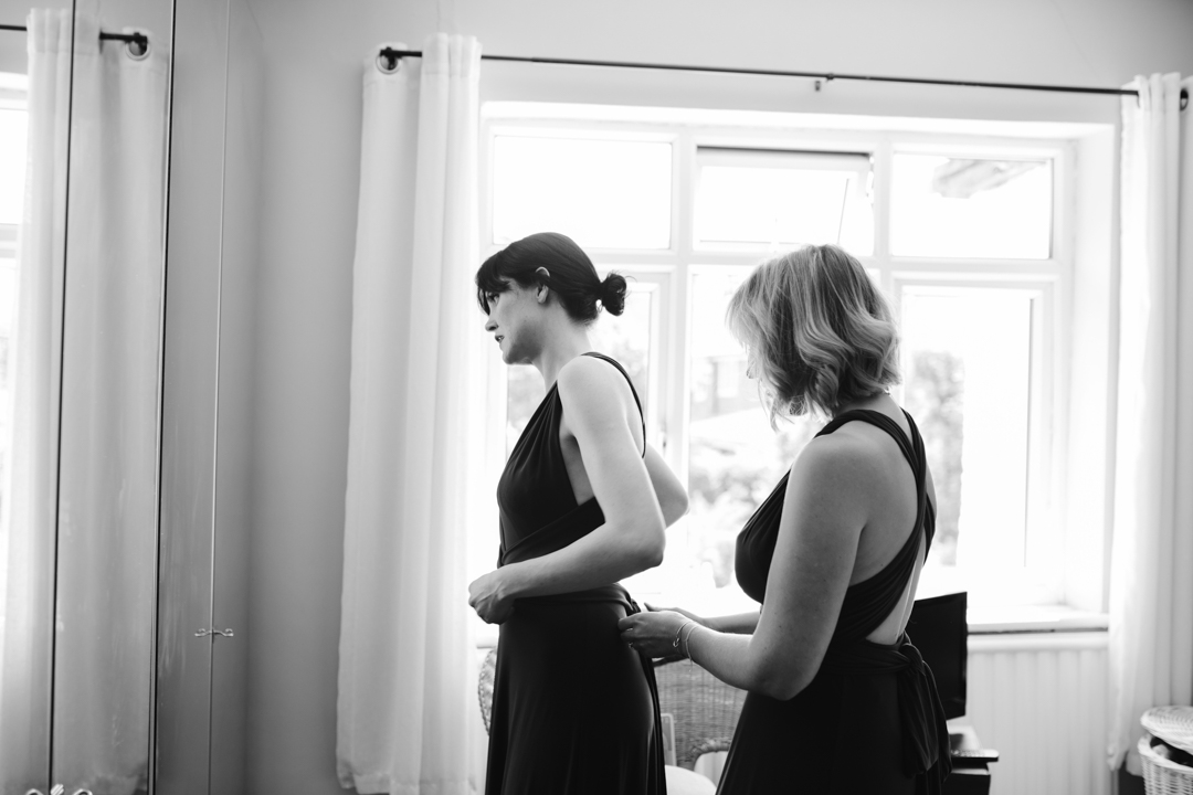 black and white photo of bridesmaids tying up each others dress 