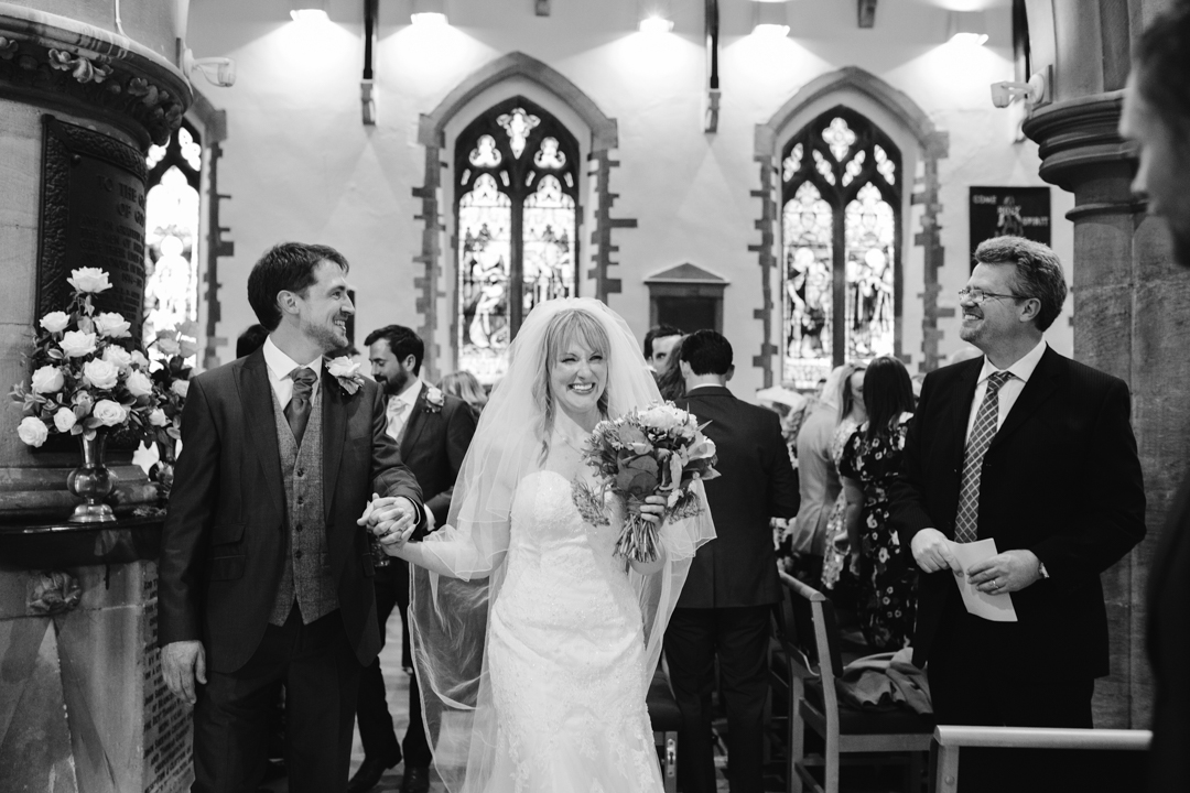 black and white natural photo of bride and groom walking down the aisle after becoming husband and wife 