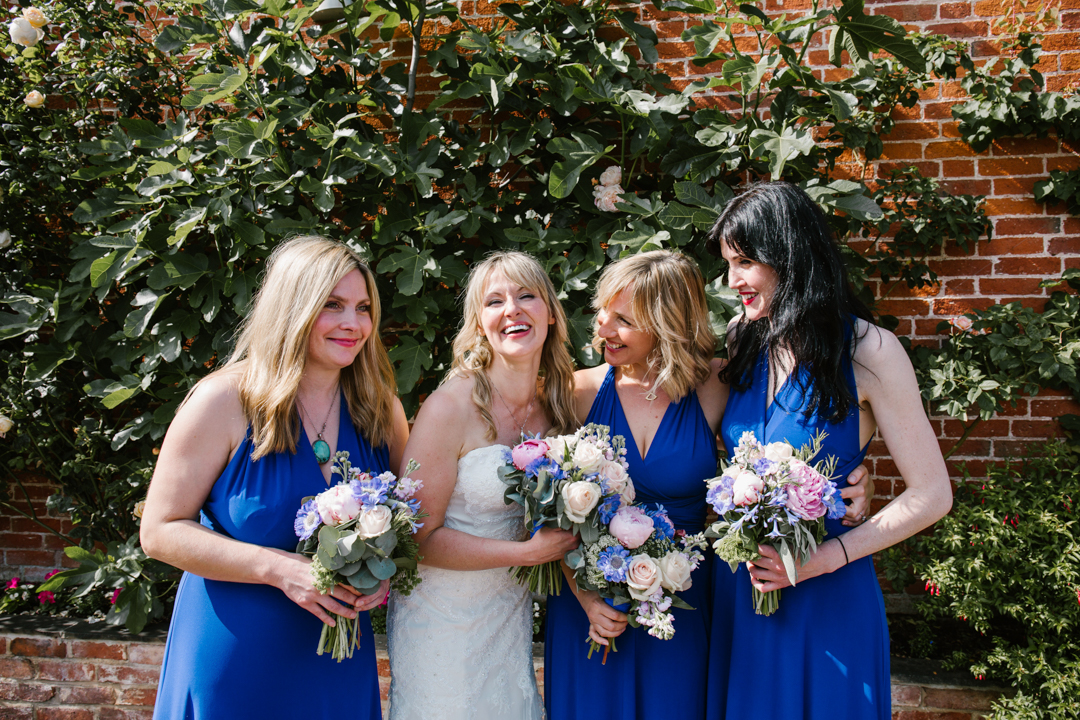 natural photo of bride and bridesmaids dressed in navy blue, laughing together in the courtyard at the walled garden in beeston fields 