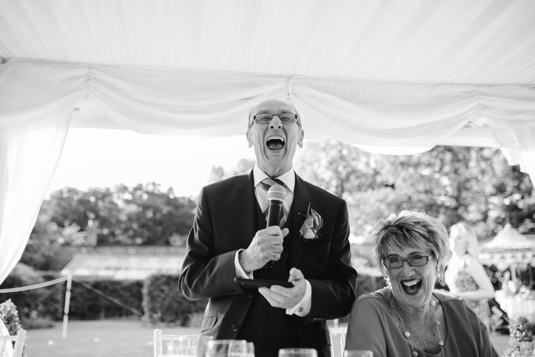 fun black and white photo of father of the bride laughing while reading his speech