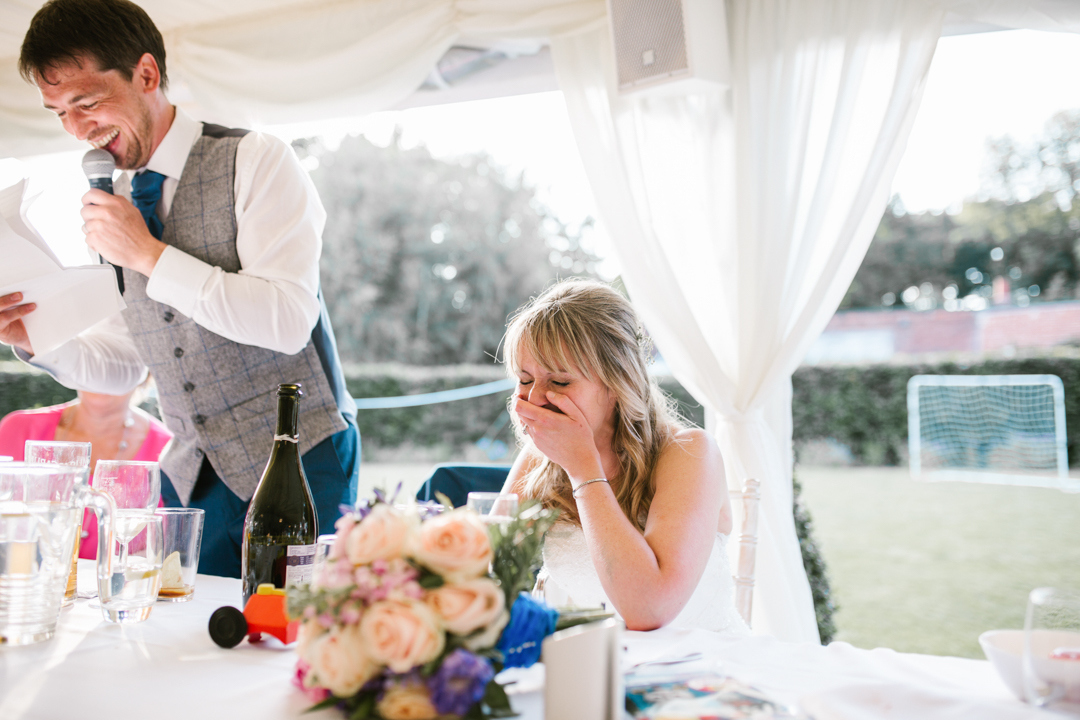 bright and natural photo of bride laughing while the groom does his wedding speech