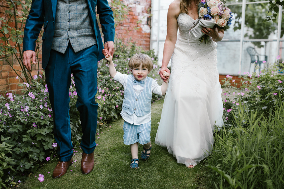 son walking hand in hand with his mom and dad in the gardens of the walled garden- nottingham wedding